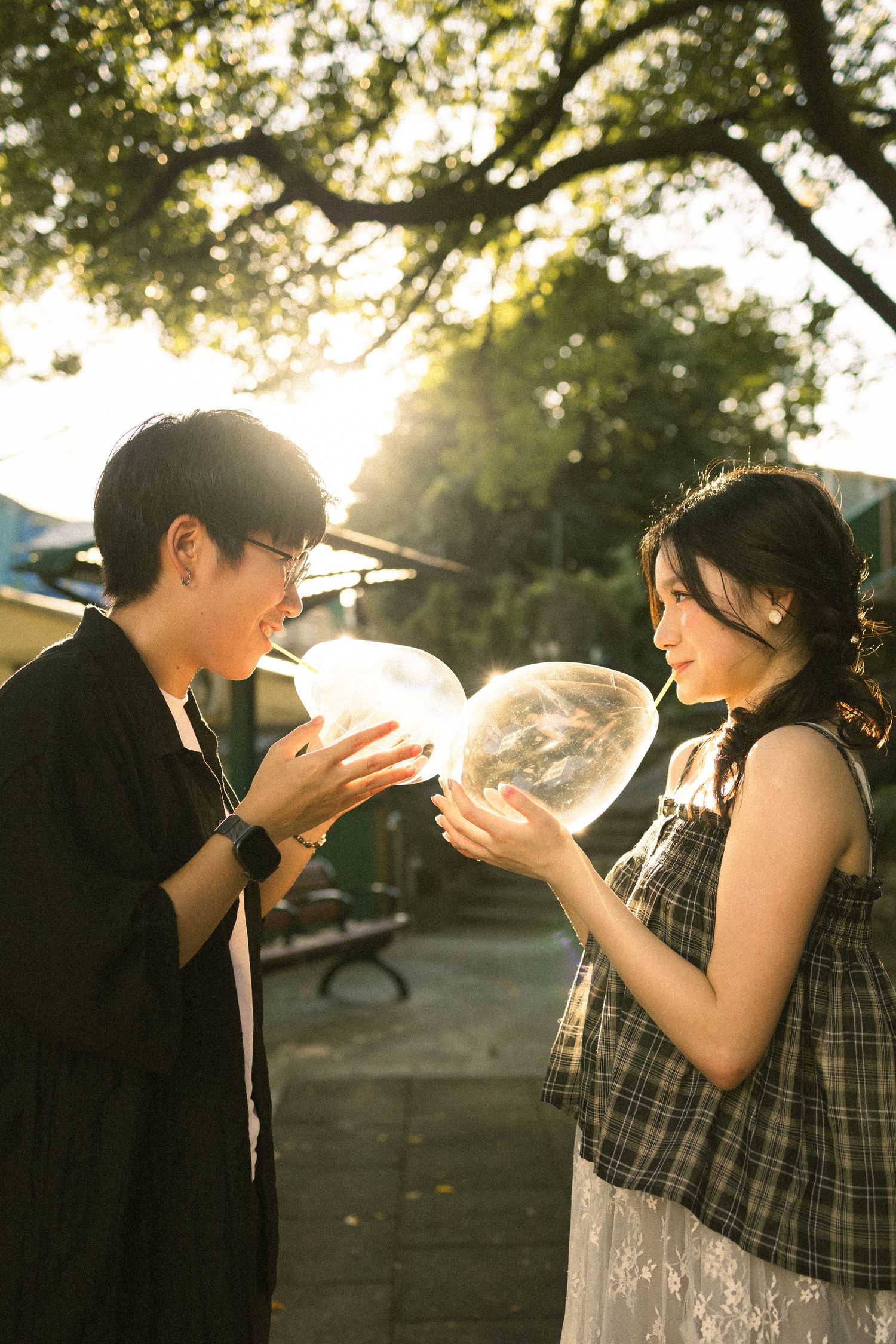 Couple sharing a glowing transparent balloon in golden sunset light among trees outdoors.