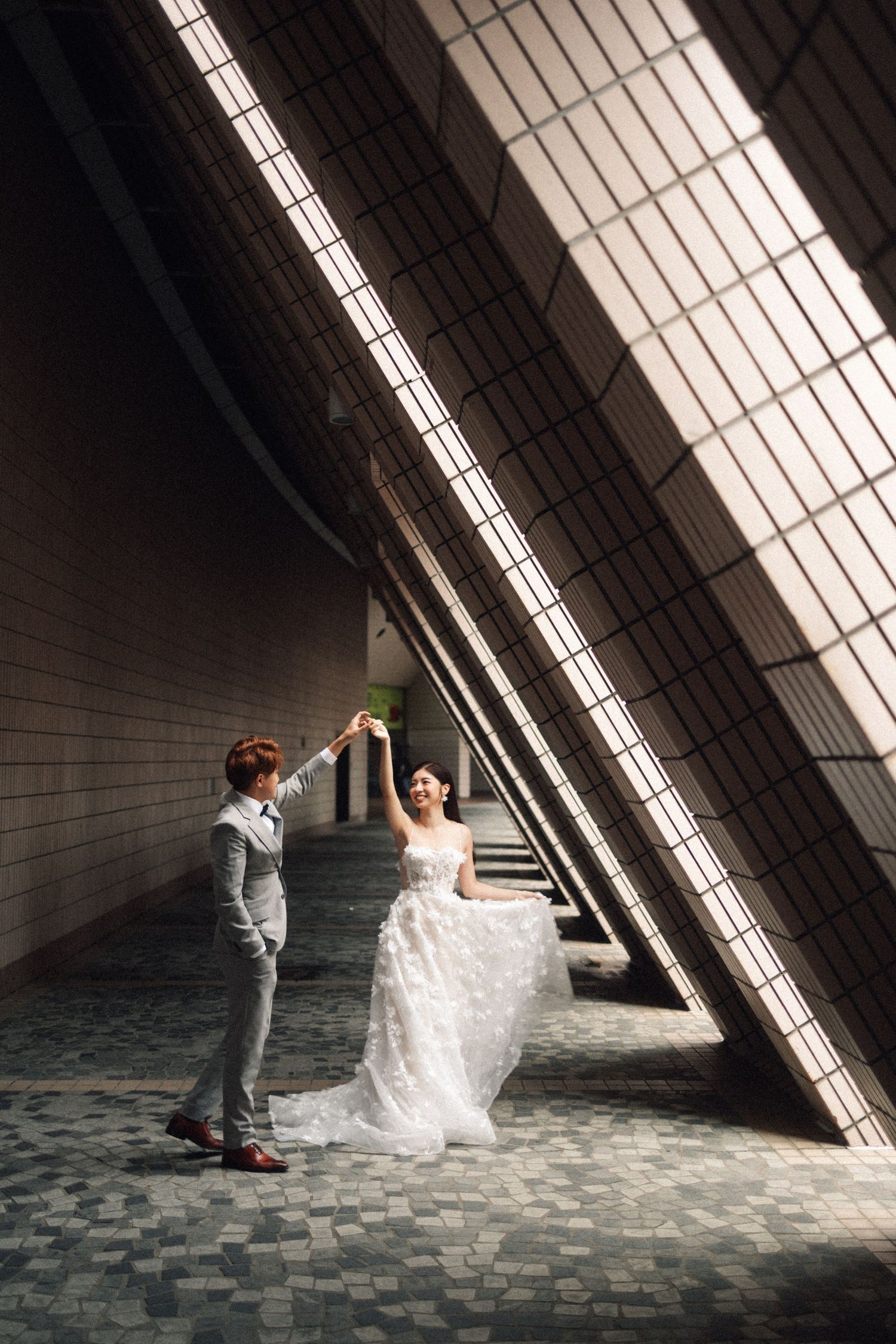 Bride and groom dance elegantly in a dramatic architectural space with diagonal light beams.