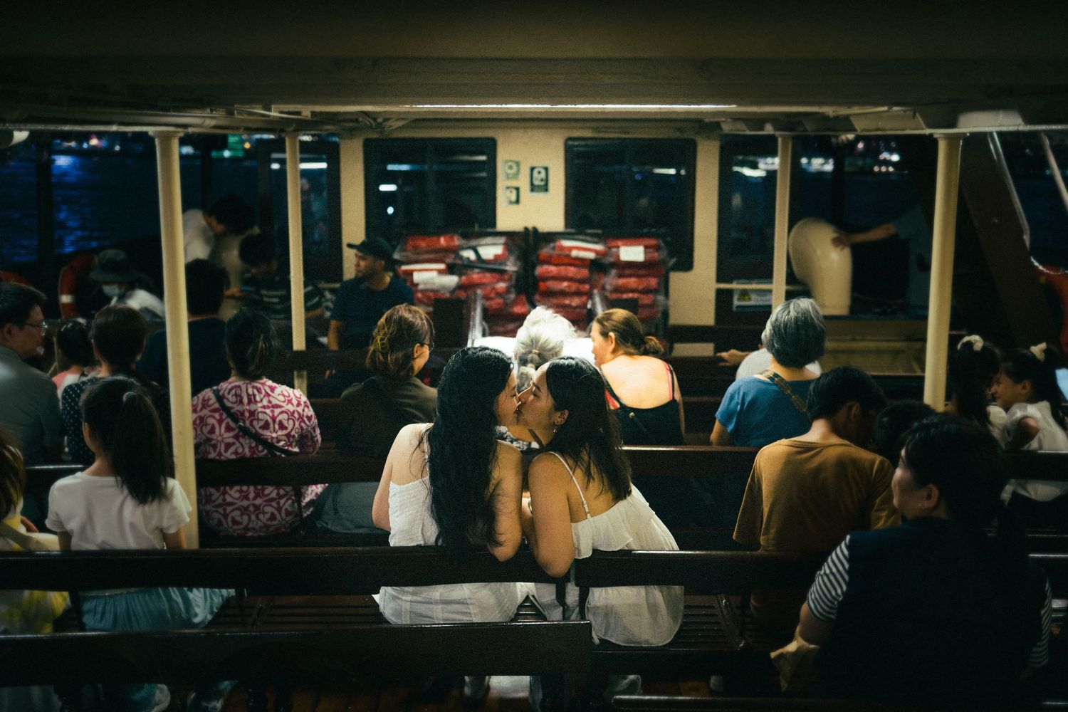 Passengers seated on a nighttime ferry ride, viewed from behind in warm interior lighting.