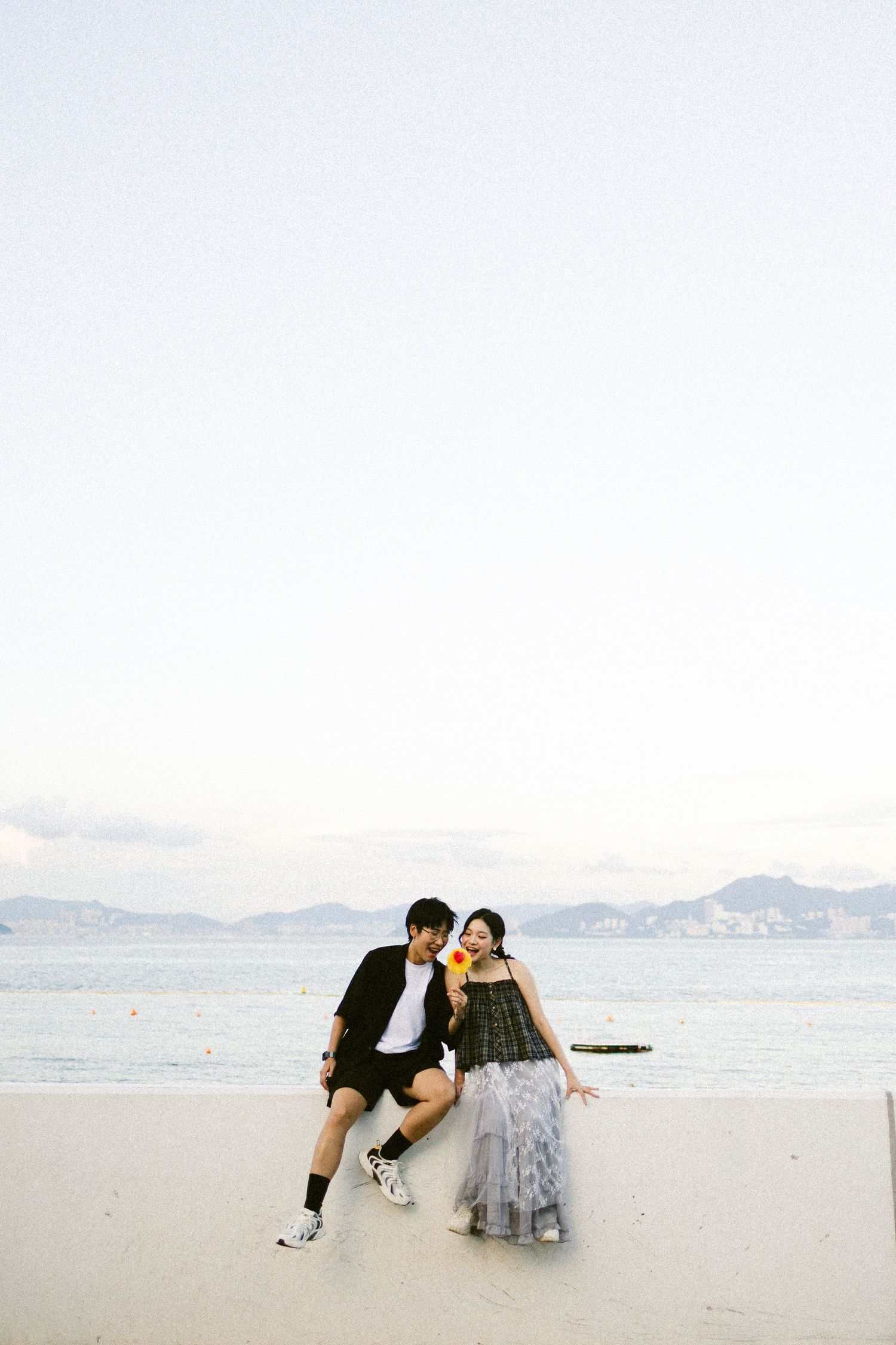 Couple sitting together on a serene sandy beach at dusk with calm ocean backdrop.