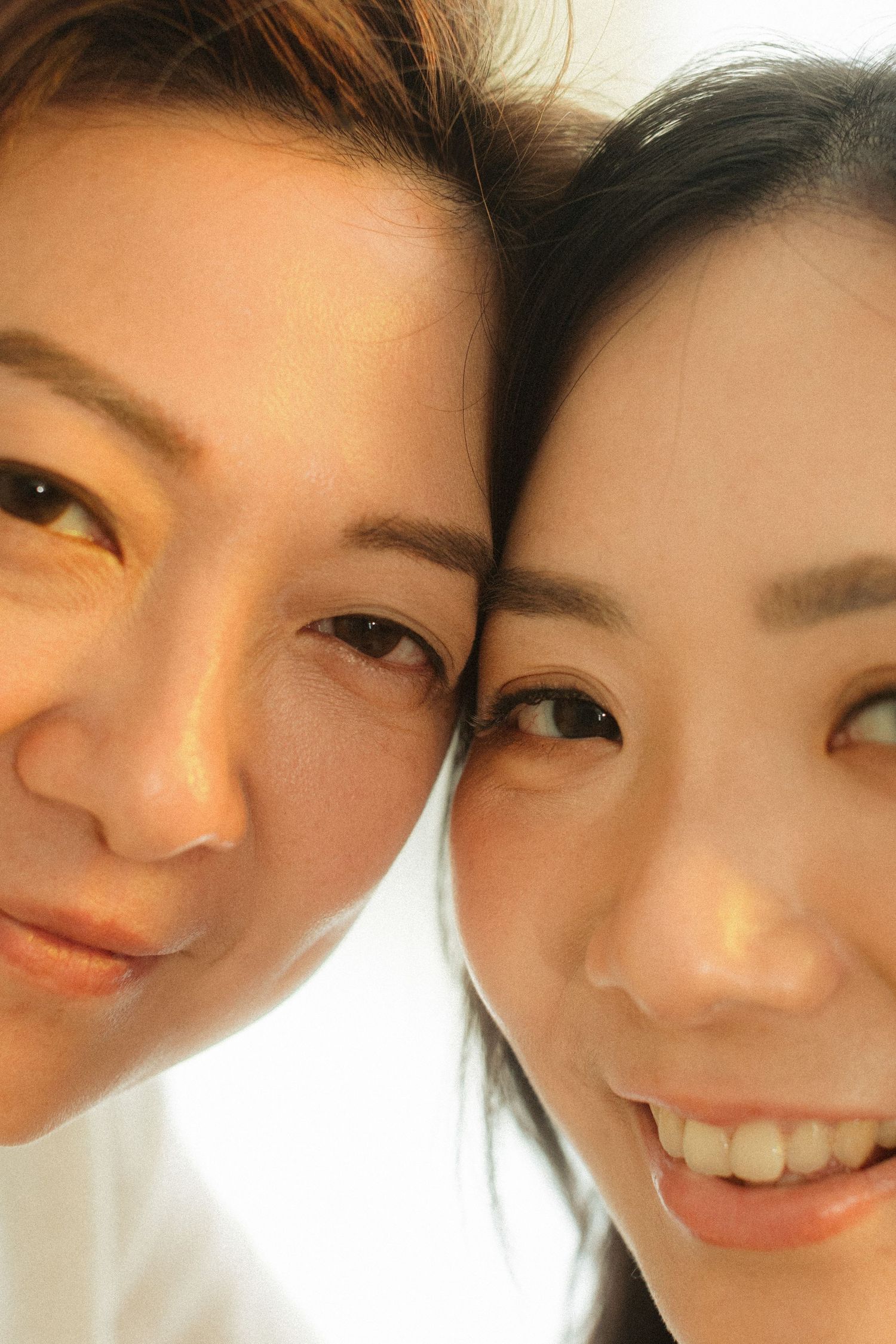 Two Asian women smiling closely together in a bright selfie portrait.