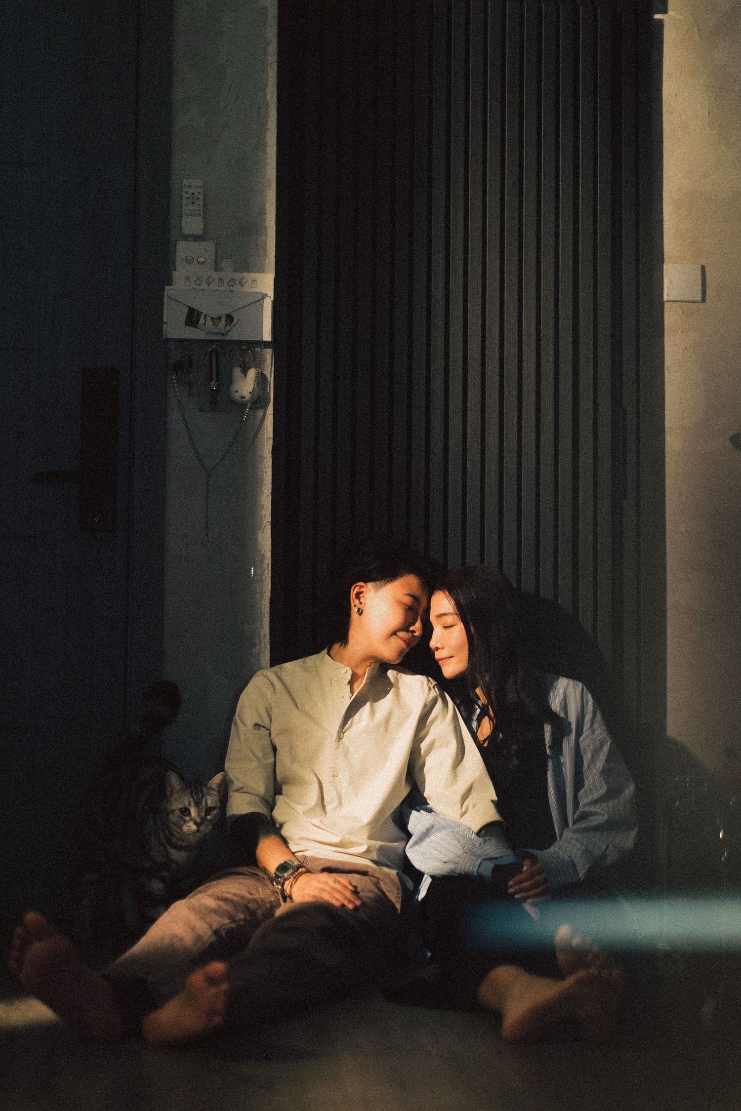 Couple sitting close together on the floor in warm sunlight with a cat beside them.