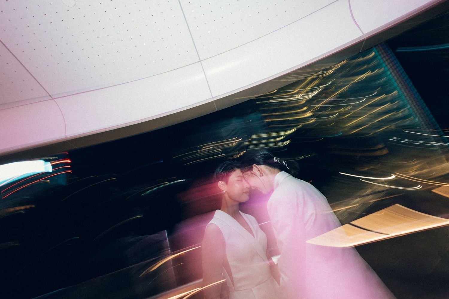 Couple sharing a kiss captured with motion blur and colorful light streaks in an urban night setting.