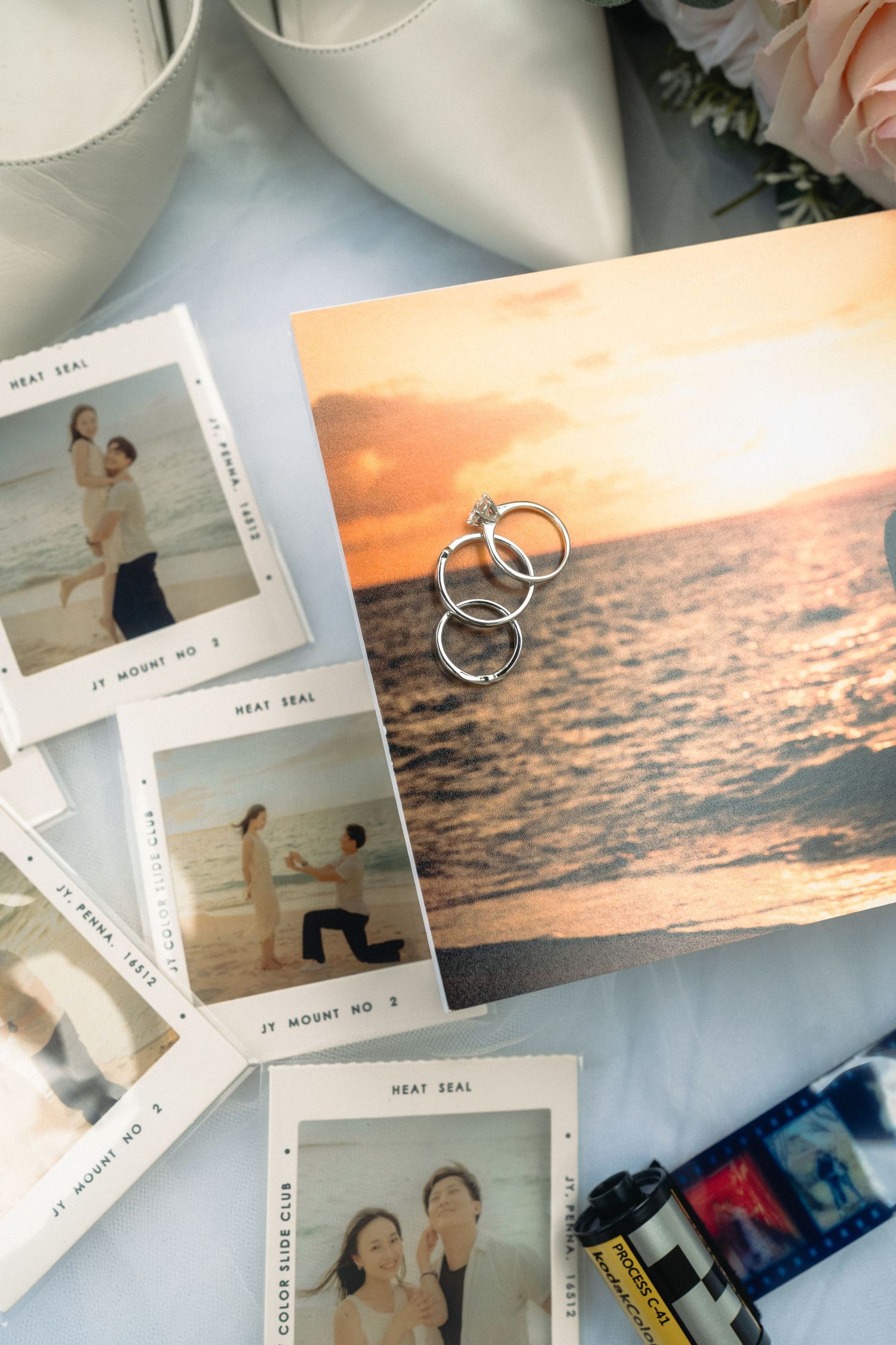 Wedding rings rest on sunset beach photo beside Polaroid engagement snapshots and bridal accessories.