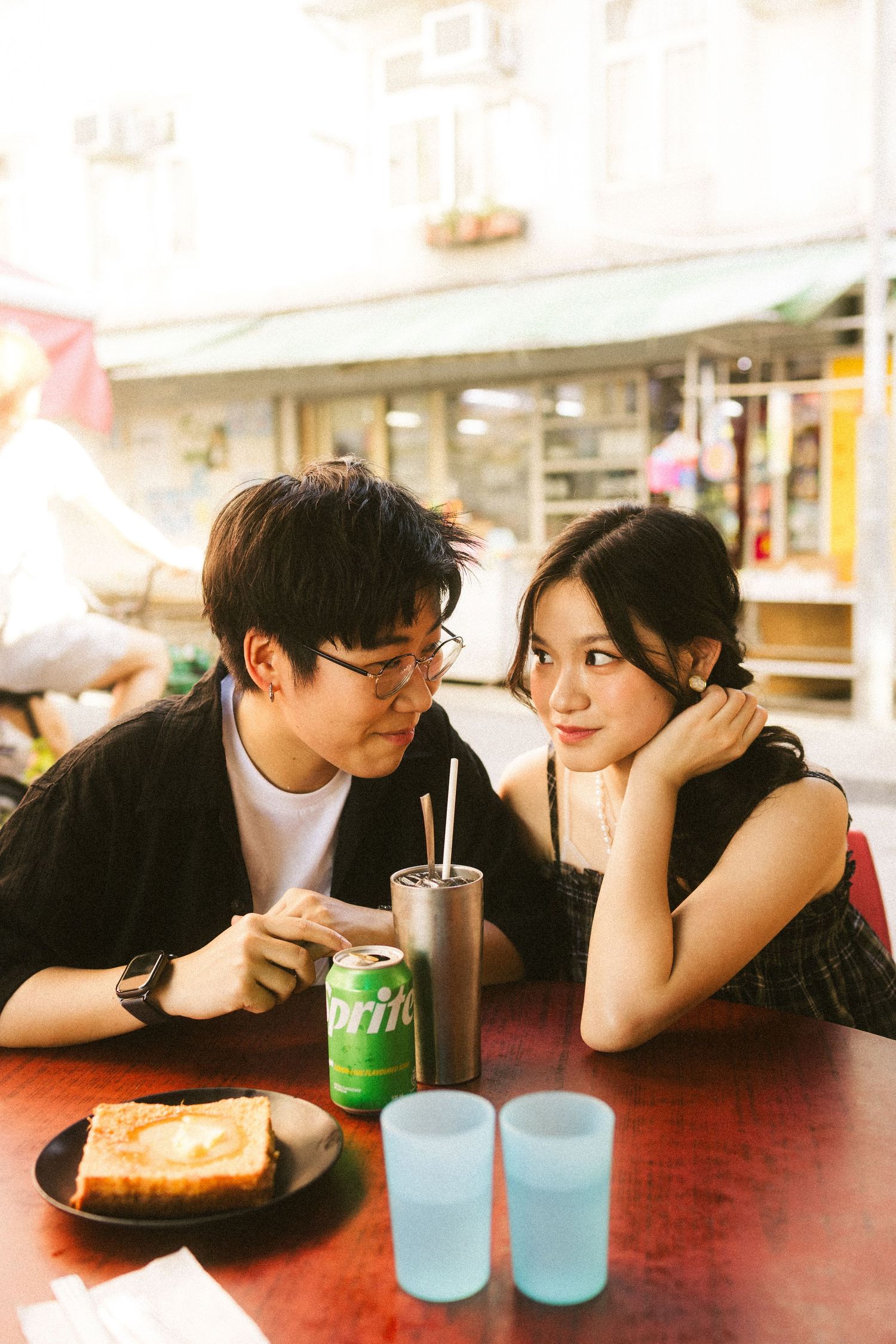 Young Asian couple gazing at each other at a red table with Sprite and toast nearby.