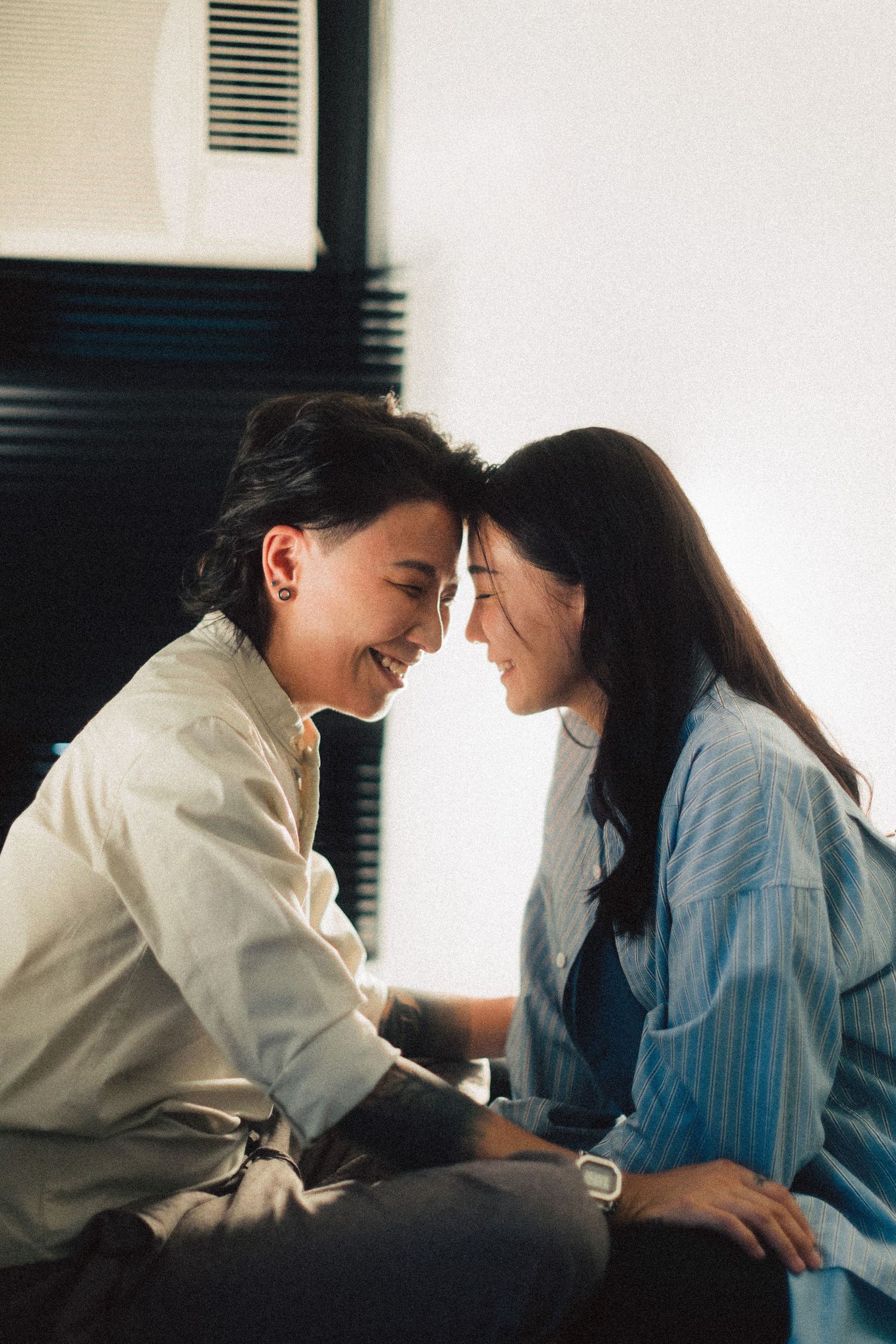 Two women laughing and touching foreheads together in bright natural indoor light.