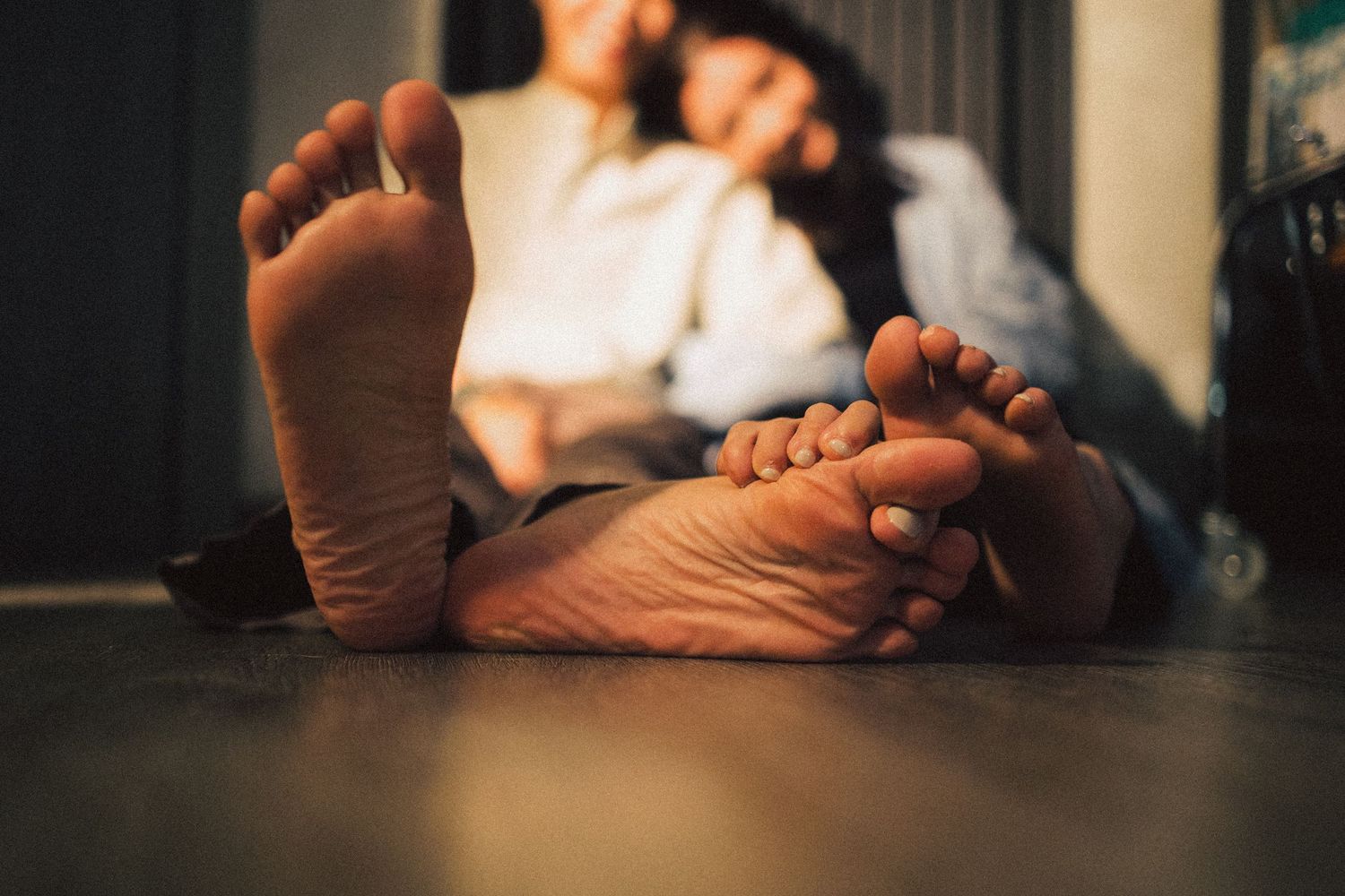 Close-up of two people's bare feet stretched out on a floor while relaxing together.