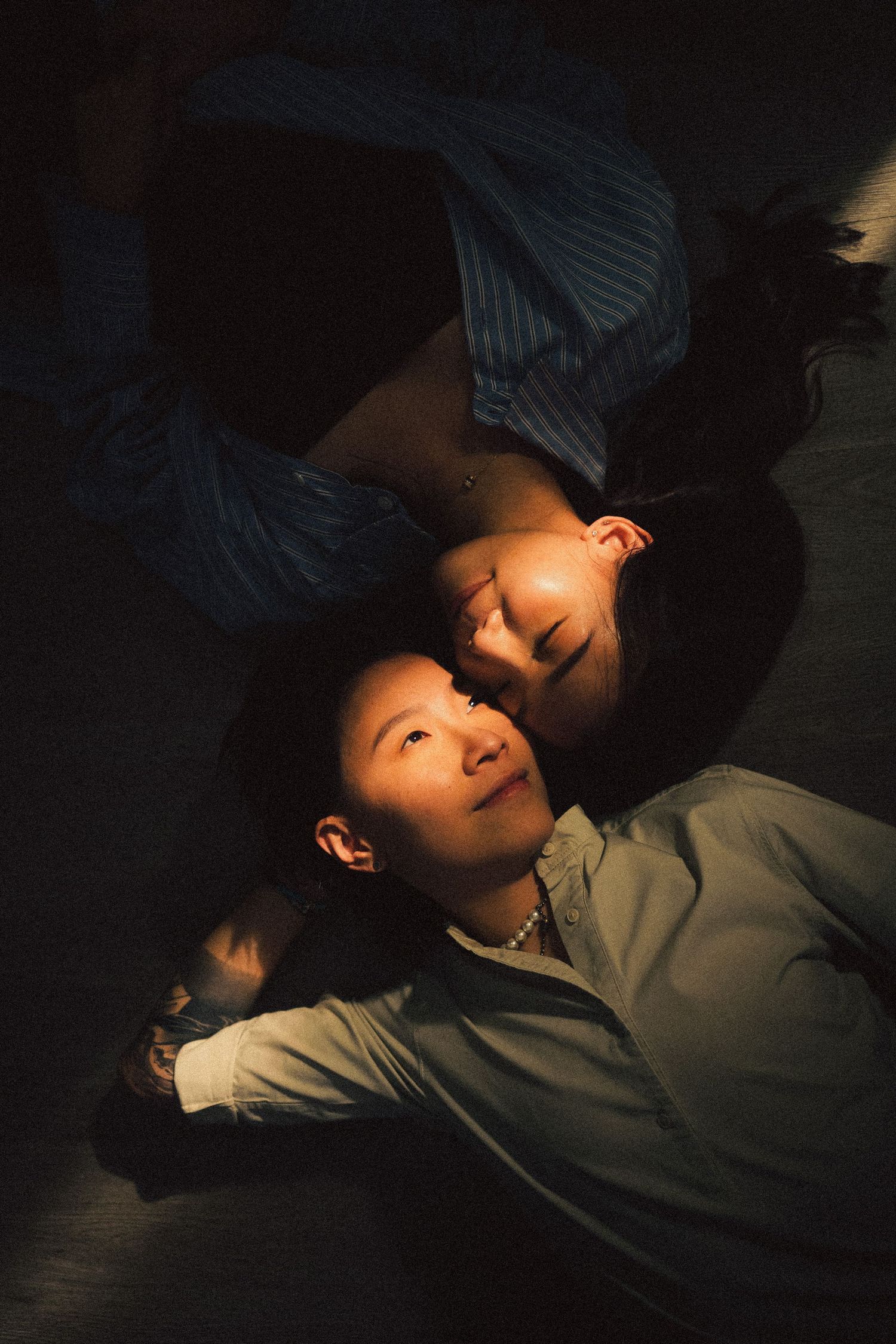 Two people lying on the floor with heads together, illuminated by warm dramatic light.