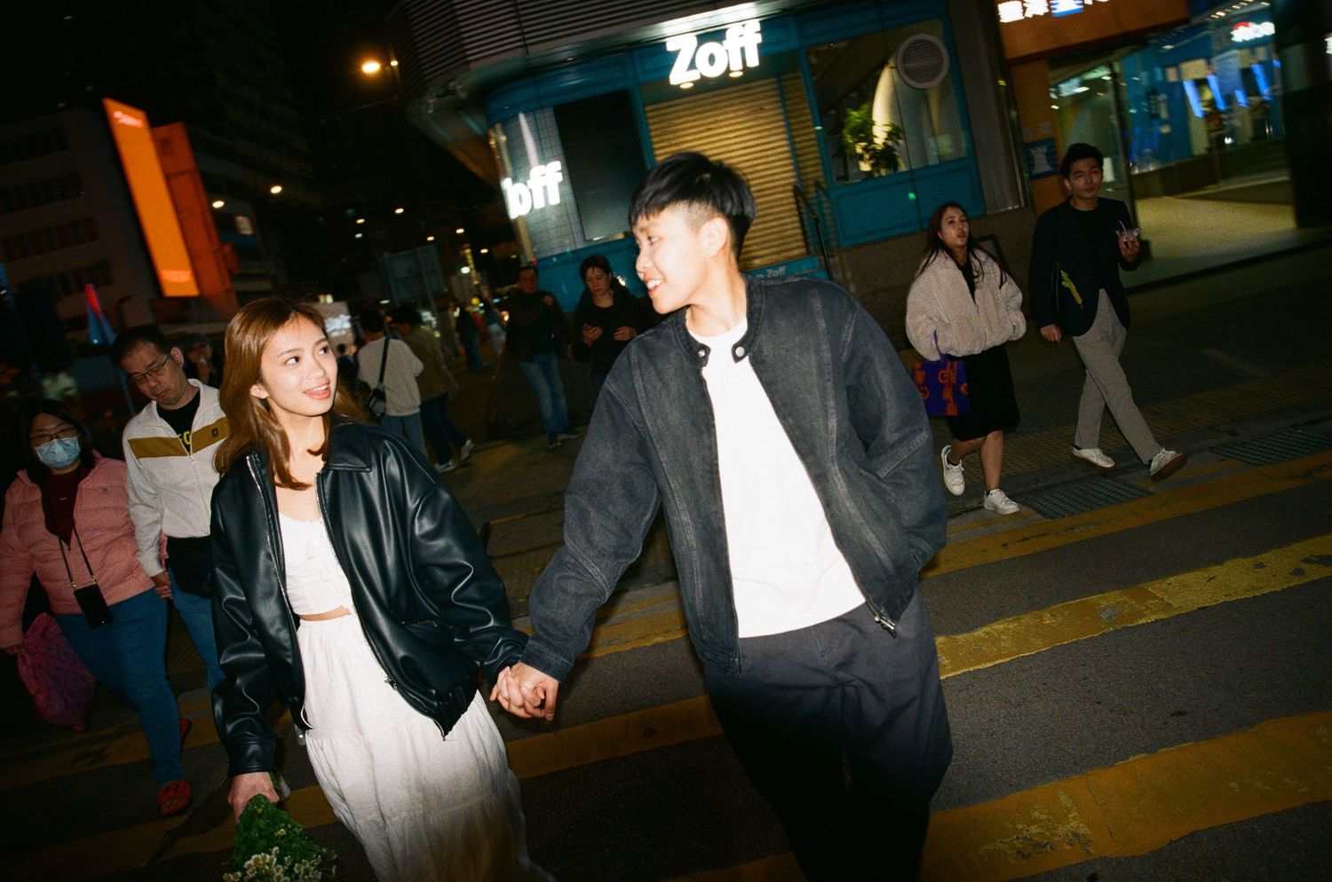 Happy couple holding hands and smiling at each other while crossing a busy street at night.