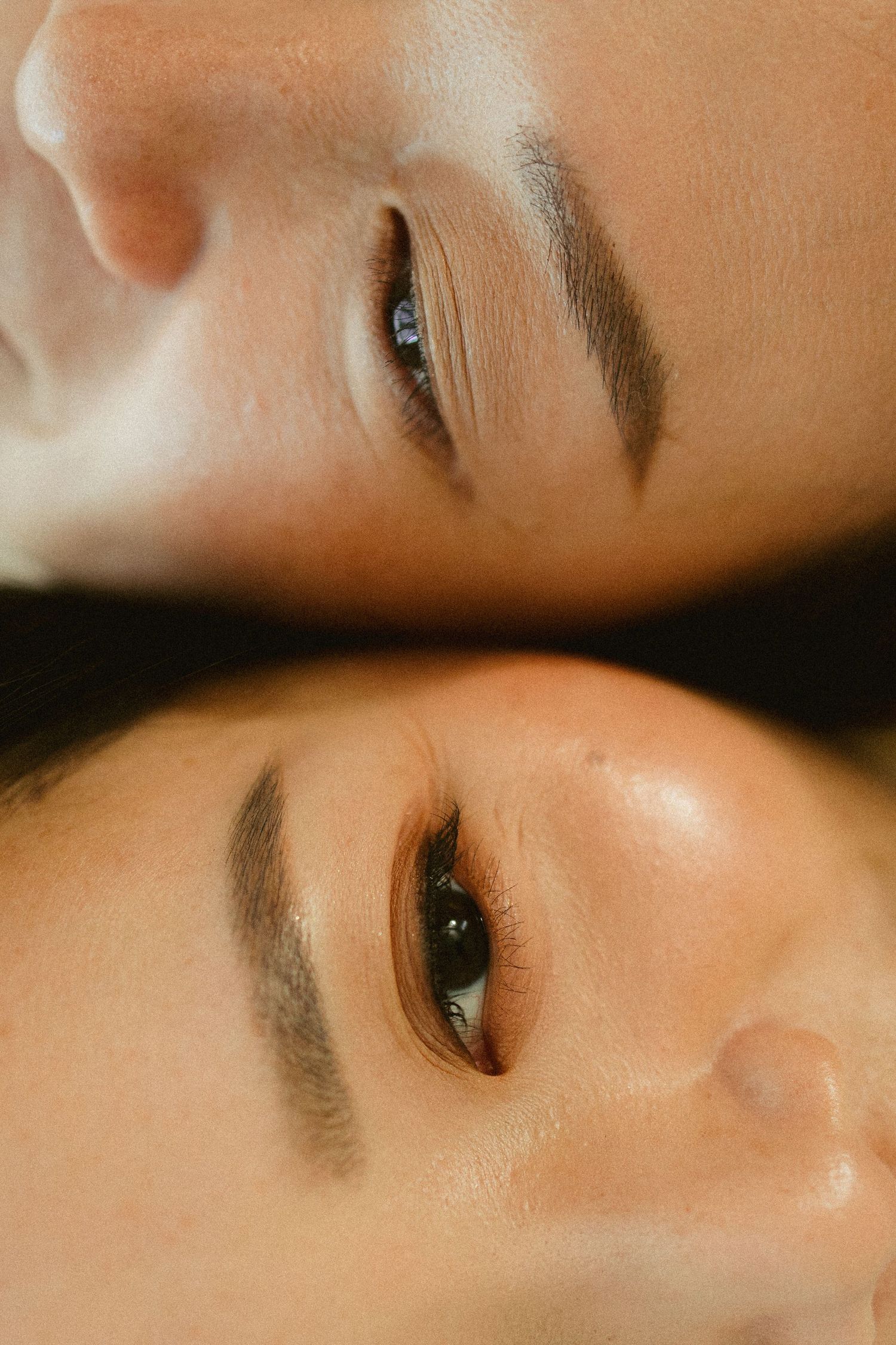 Close-up portrait of two faces positioned head-to-head, showcasing natural skin and defined eyebrows.