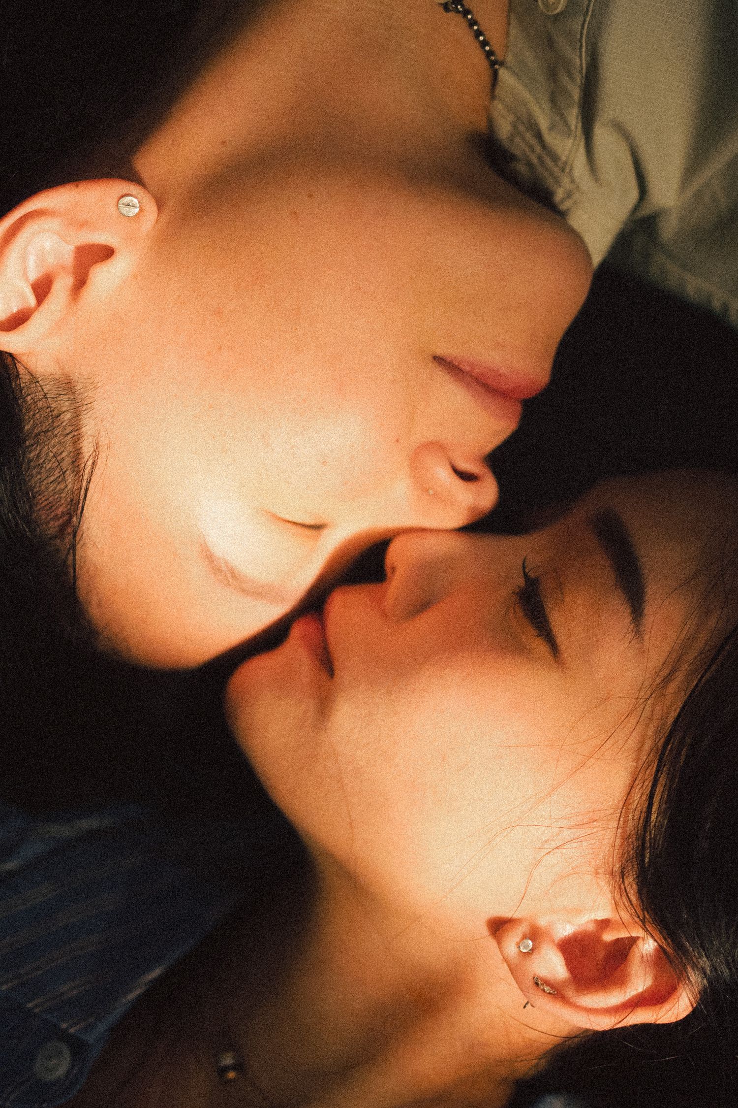 Close-up intimate portrait of two people with eyes closed, faces nearly touching in warm light.