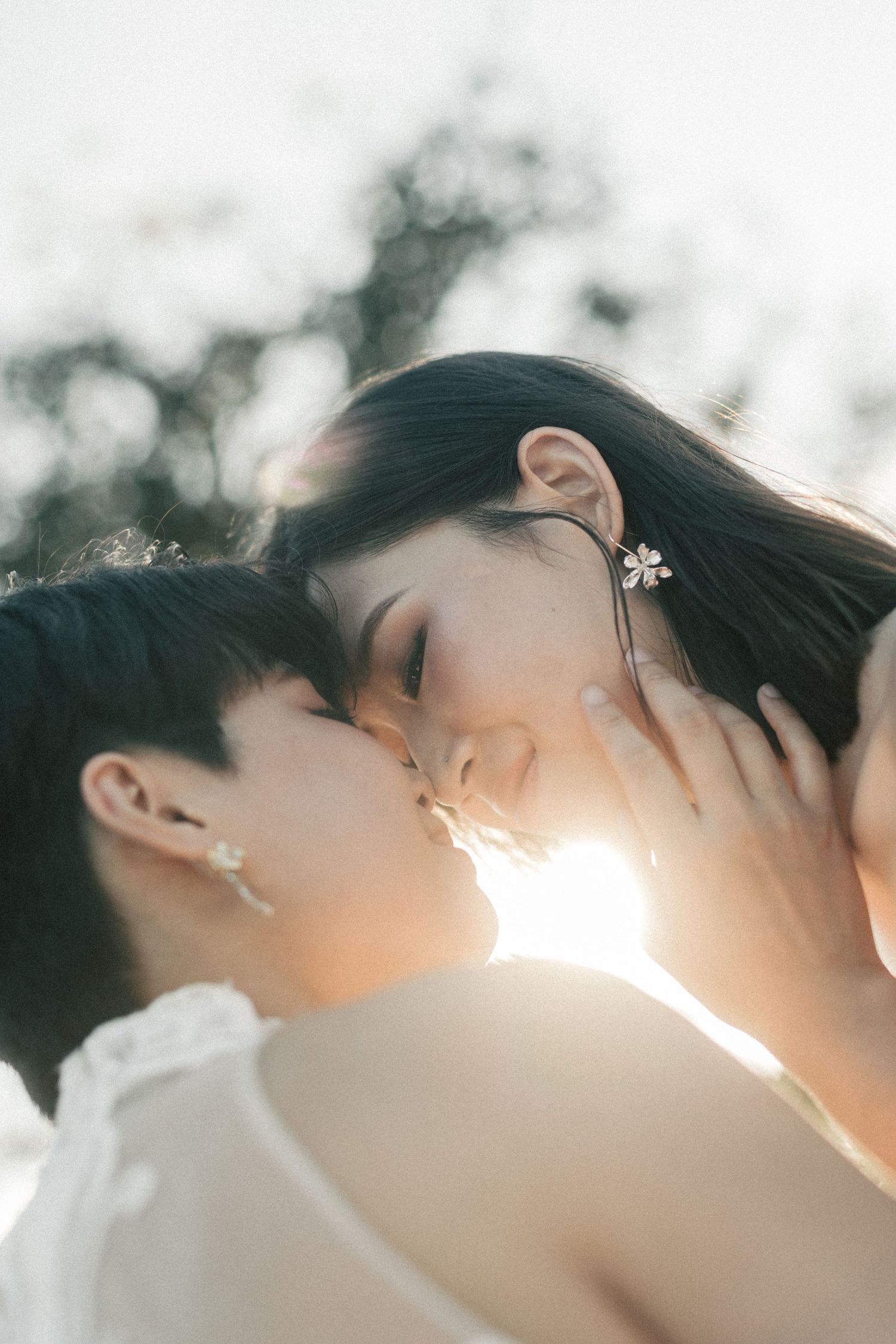 Two brides share an intimate almost-kiss bathed in warm golden backlight outdoors.