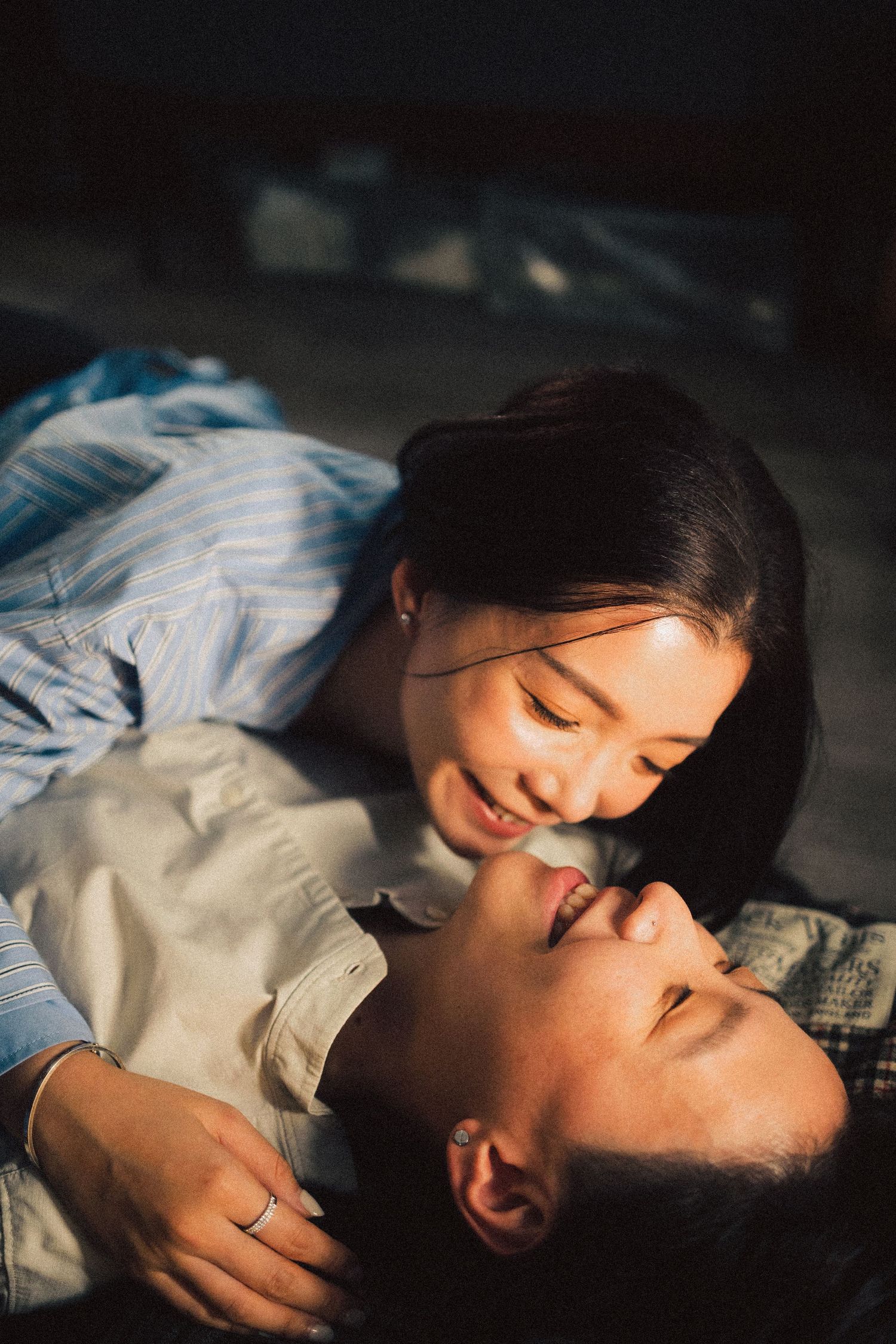 Two smiling Asian women lying close together sharing a tender romantic moment indoors.
