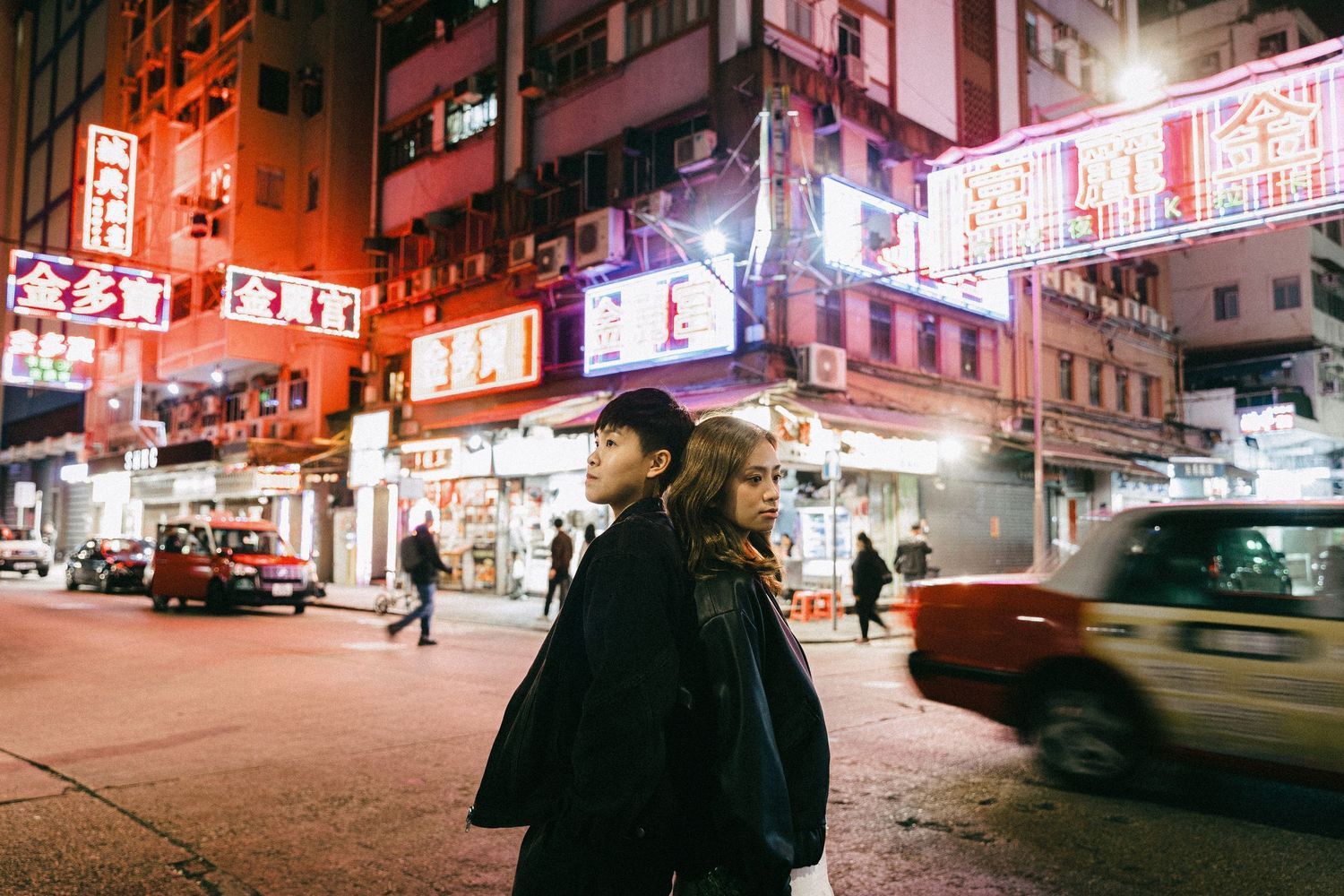 Young couple standing together on a vibrant Hong Kong street at night with colorful neon signs.