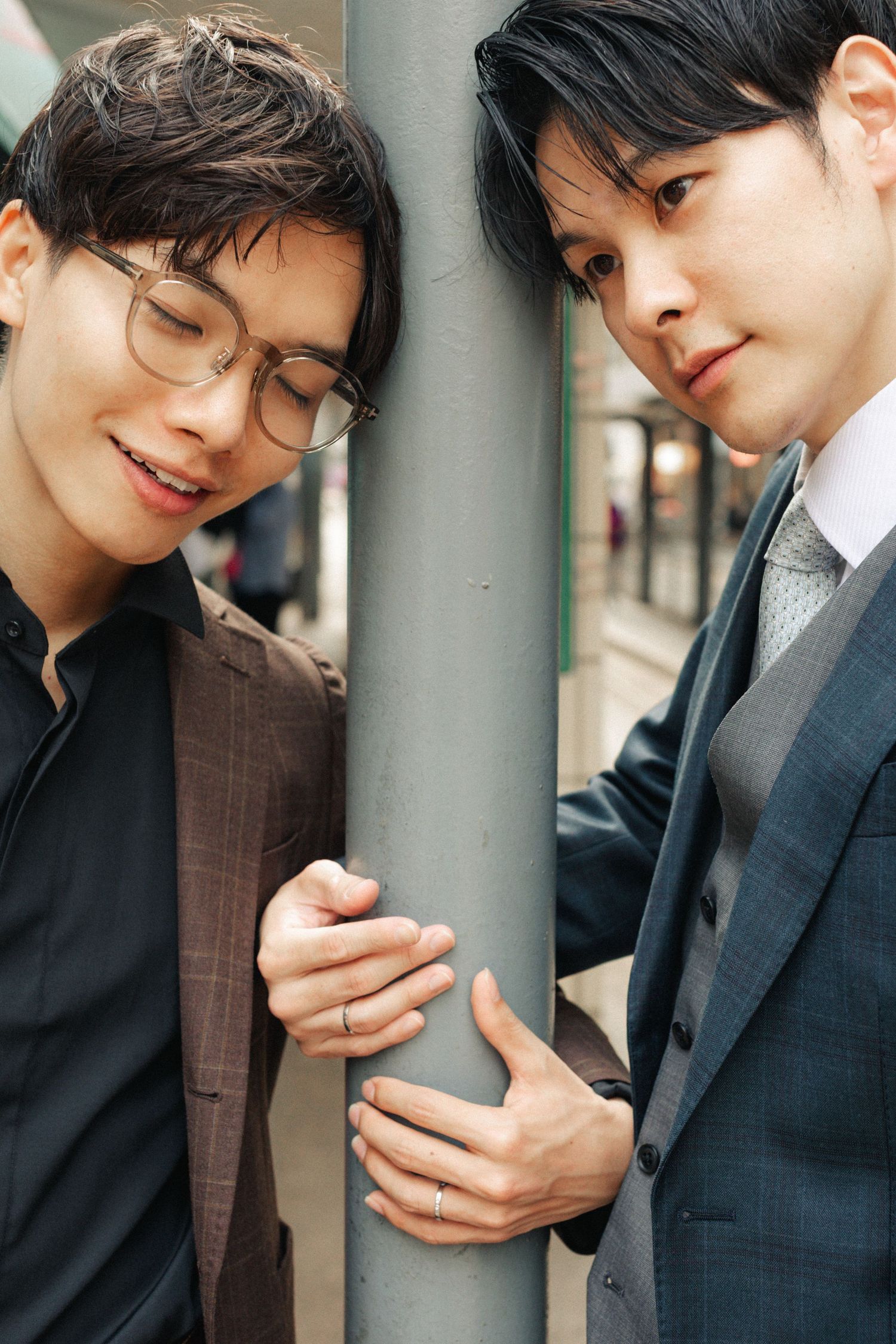 Two Asian men in suits hold a pole between them on a Hong Kong street, facing each other.