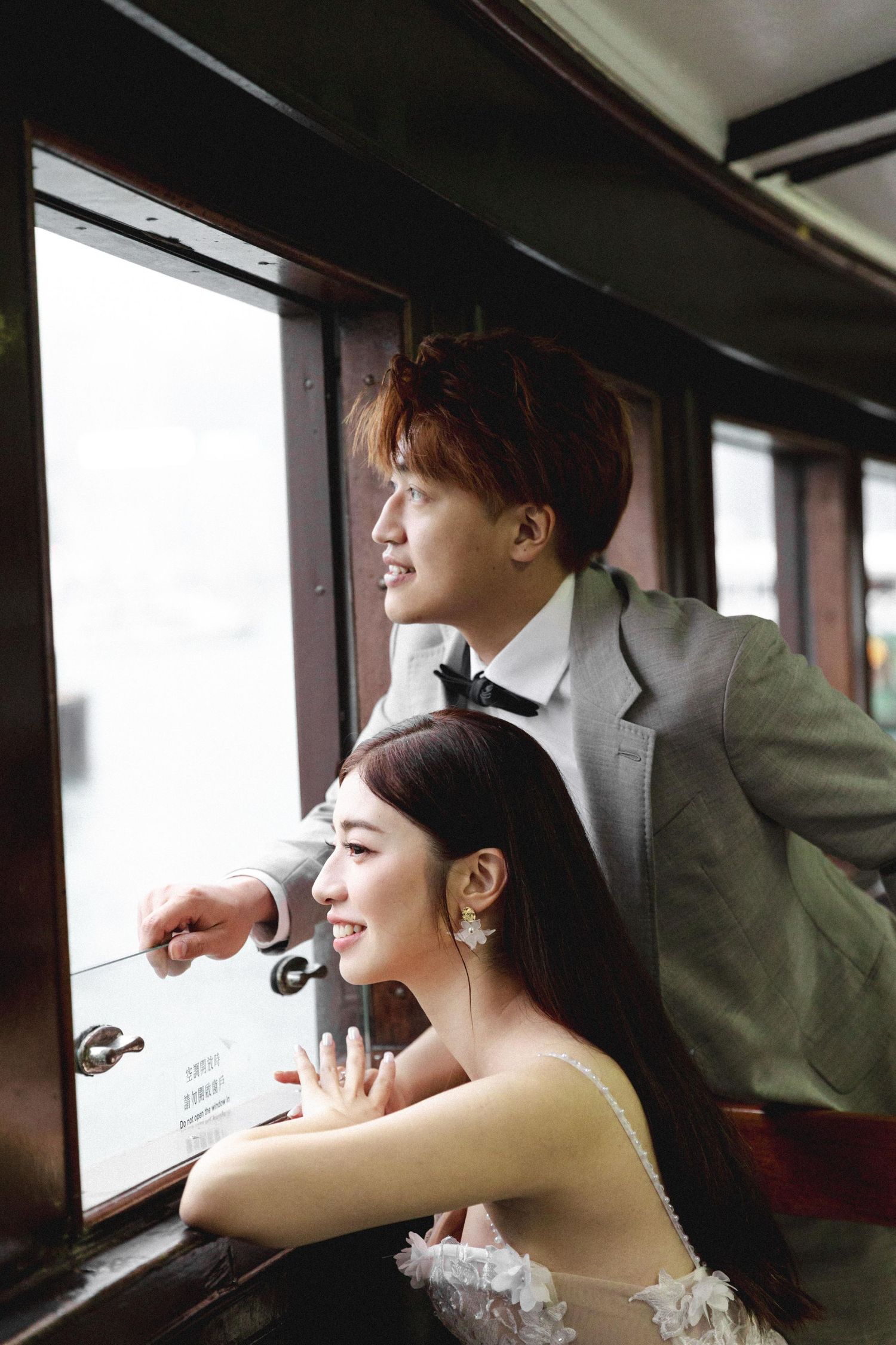Romantic couple in wedding attire gazing out a vintage tram window together in Hong Kong.