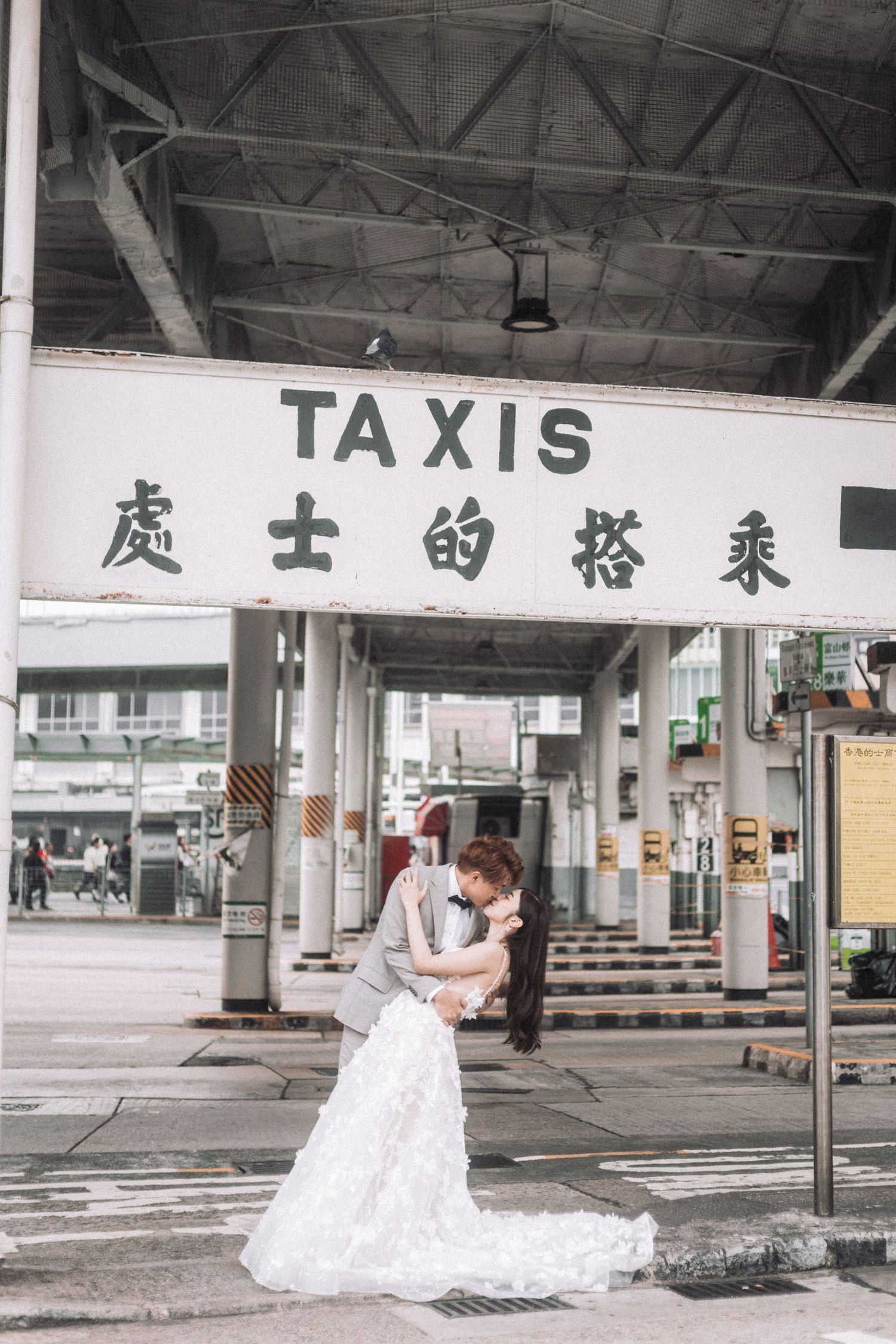 Bride and groom share a romantic dip kiss under a TAXIS sign at a Hong Kong terminal.