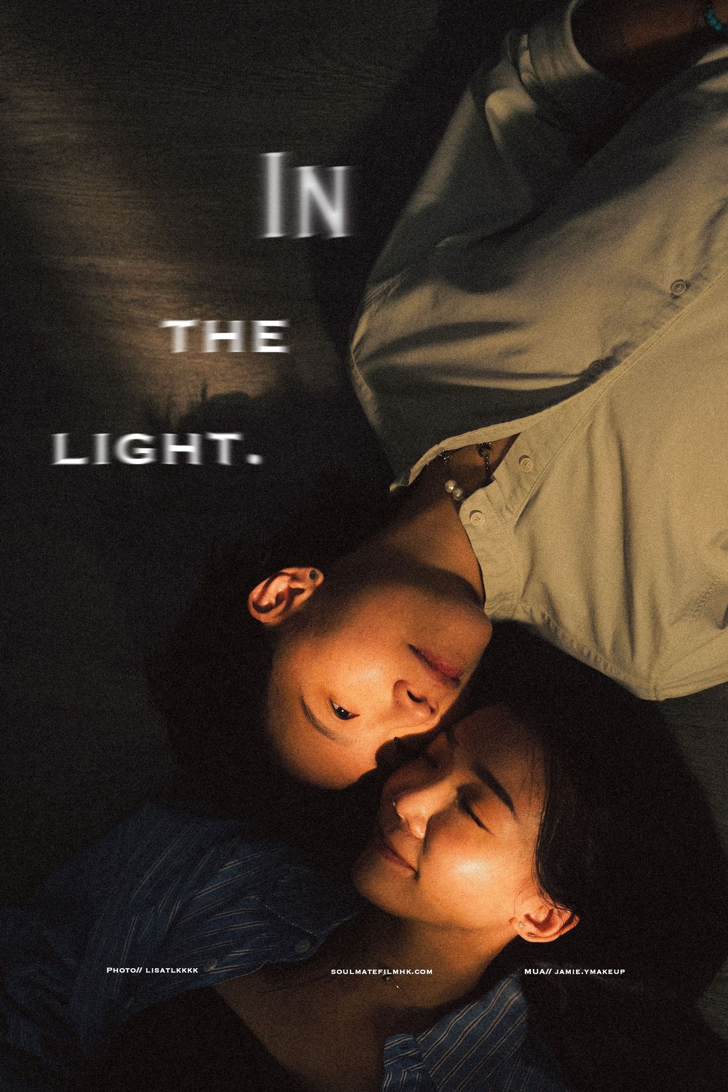 Artistic portrait of couple lying head to head under dramatic light with In The Light text overlay.