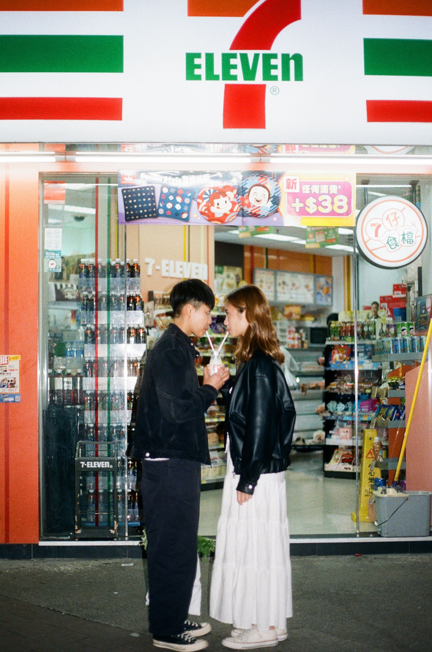Young couple facing each other in front of a brightly lit 7-Eleven convenience store at night.