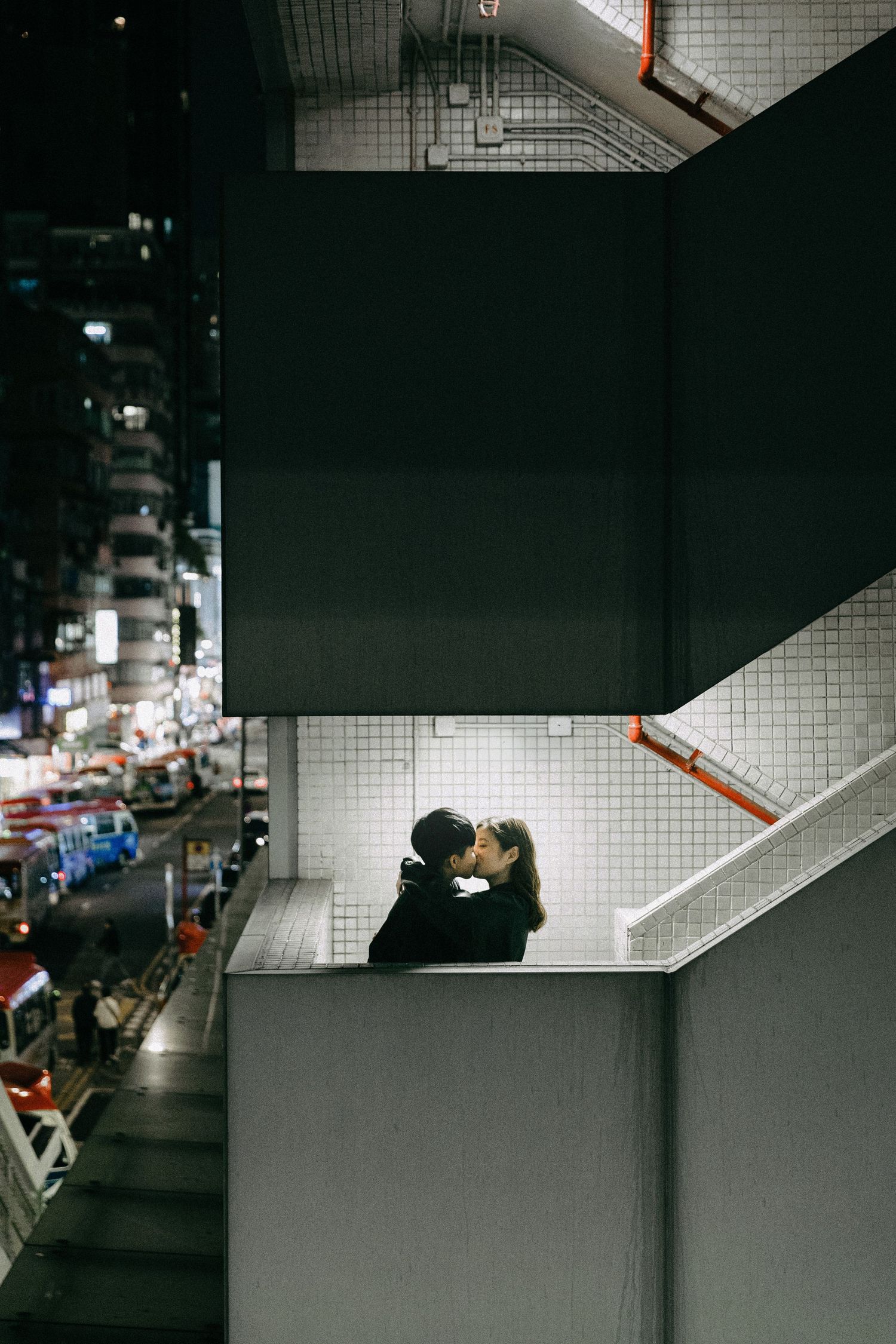 A couple sharing a kiss on an urban staircase overlooking a busy city street at night.