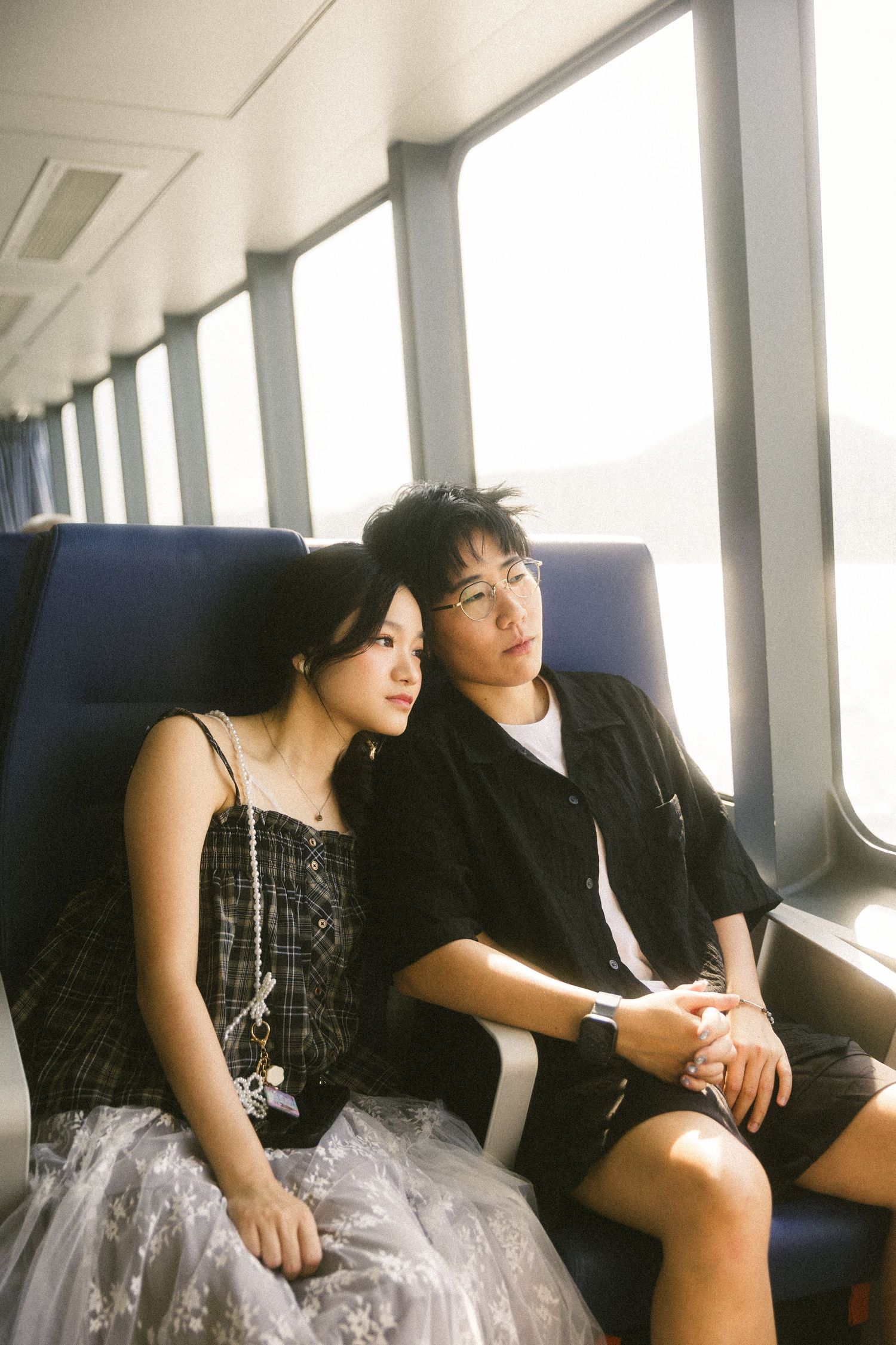 Young Asian couple holding hands and gazing out the window while seated on a ferry.