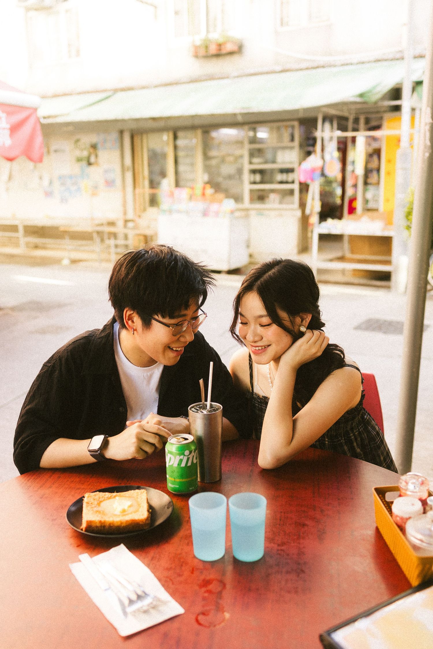 Young Asian couple sharing a joyful moment at an outdoor cafe table with toast and drinks.