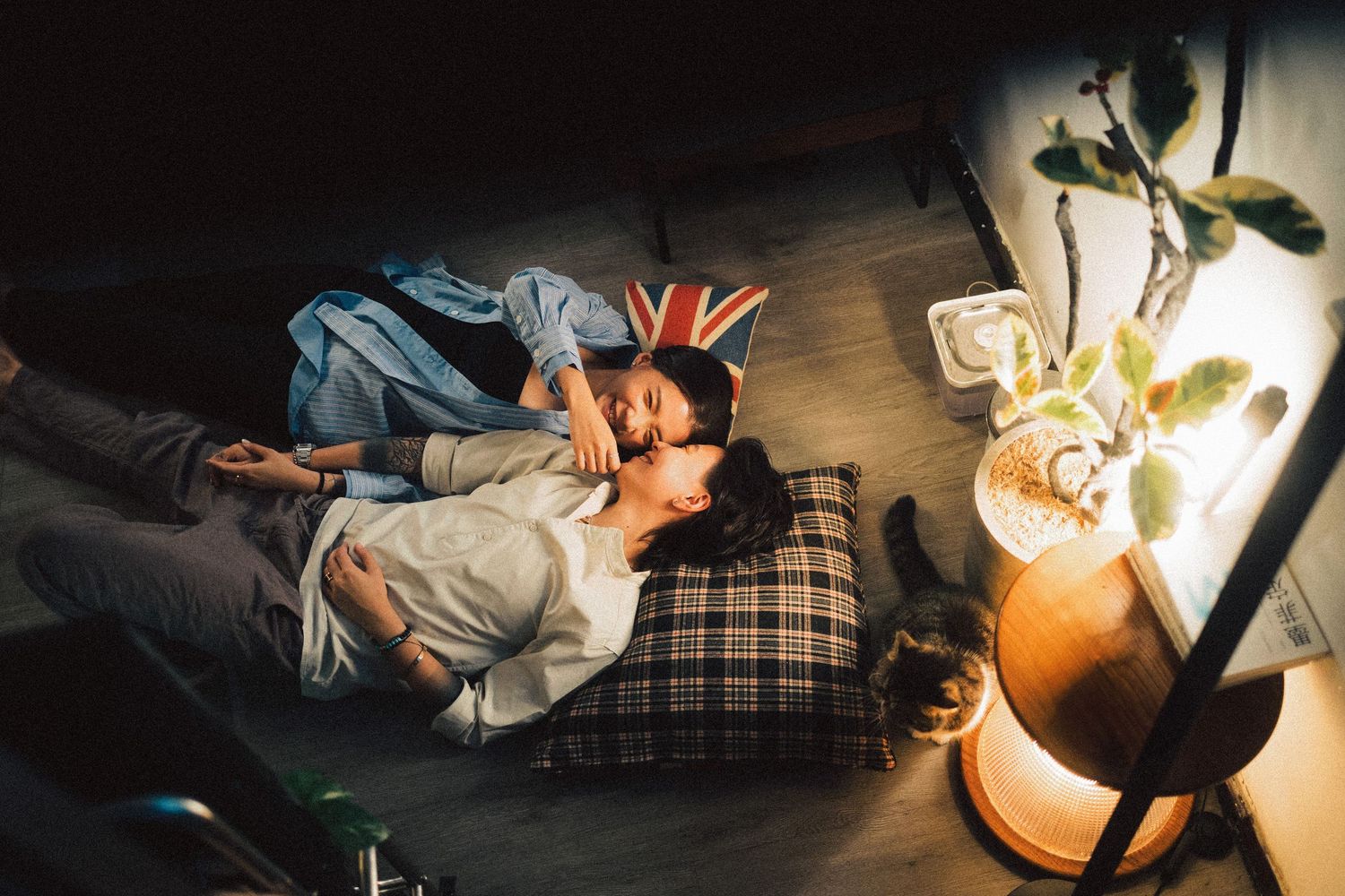 Couple lying on floor cushions in dim living room, sharing an intimate moment together at night.