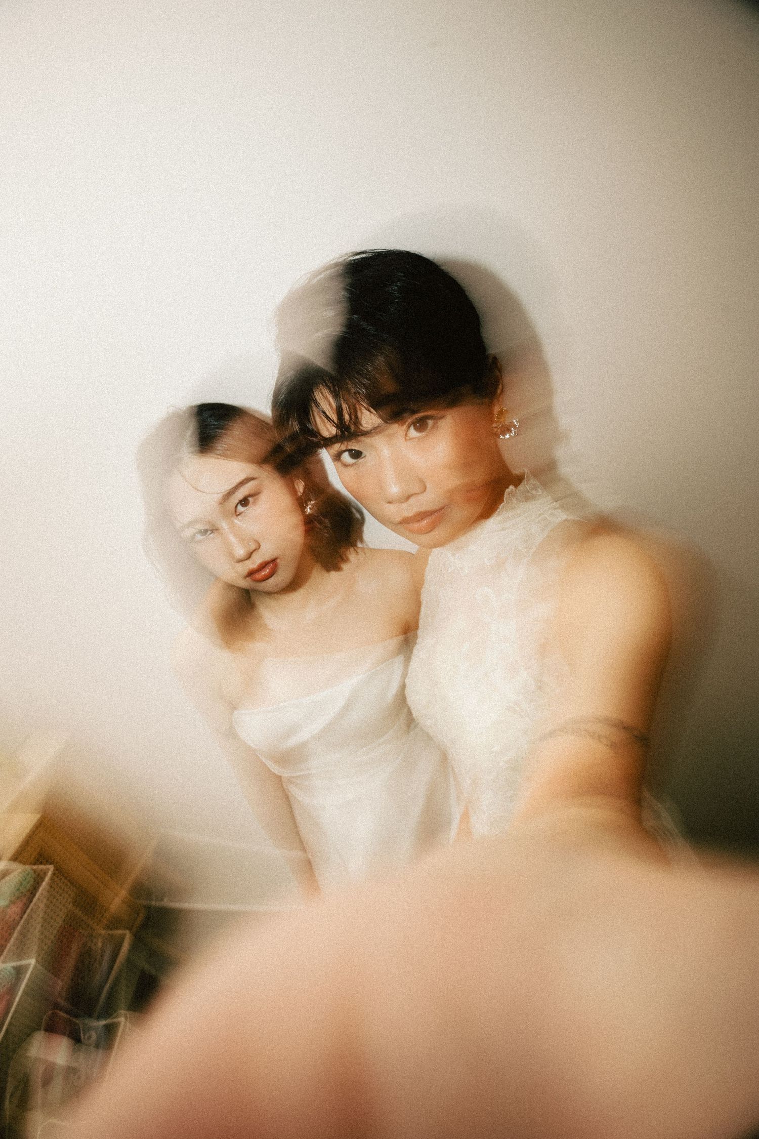 An artistic double-exposure portrait of two Asian brides in white gowns creates a dreamy, ethereal effect.