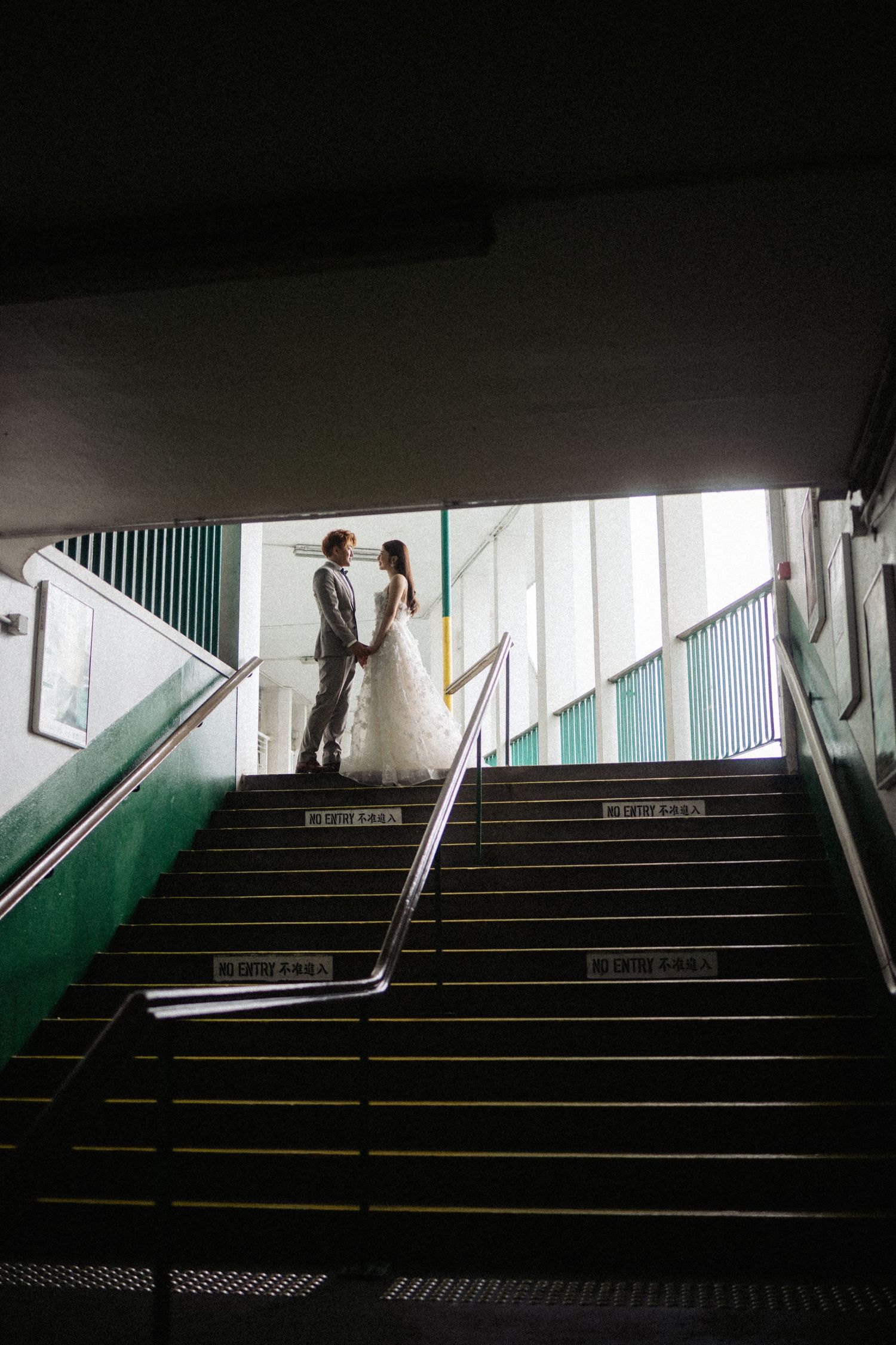 Bride and groom hold hands at top of dramatic staircase with green railings in silhouette.