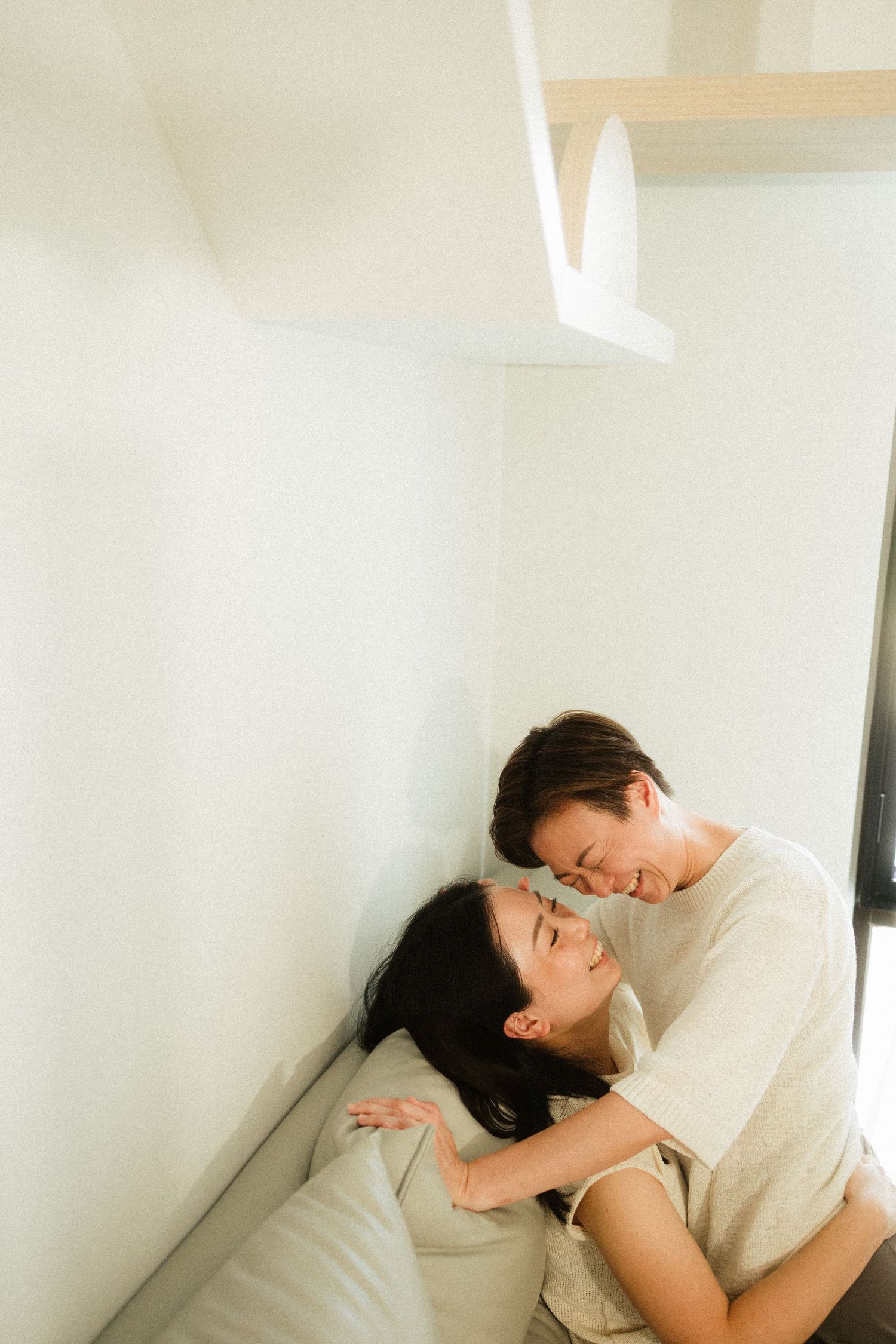 Asian couple sharing a close romantic moment while nestled in a bright white cozy corner.
