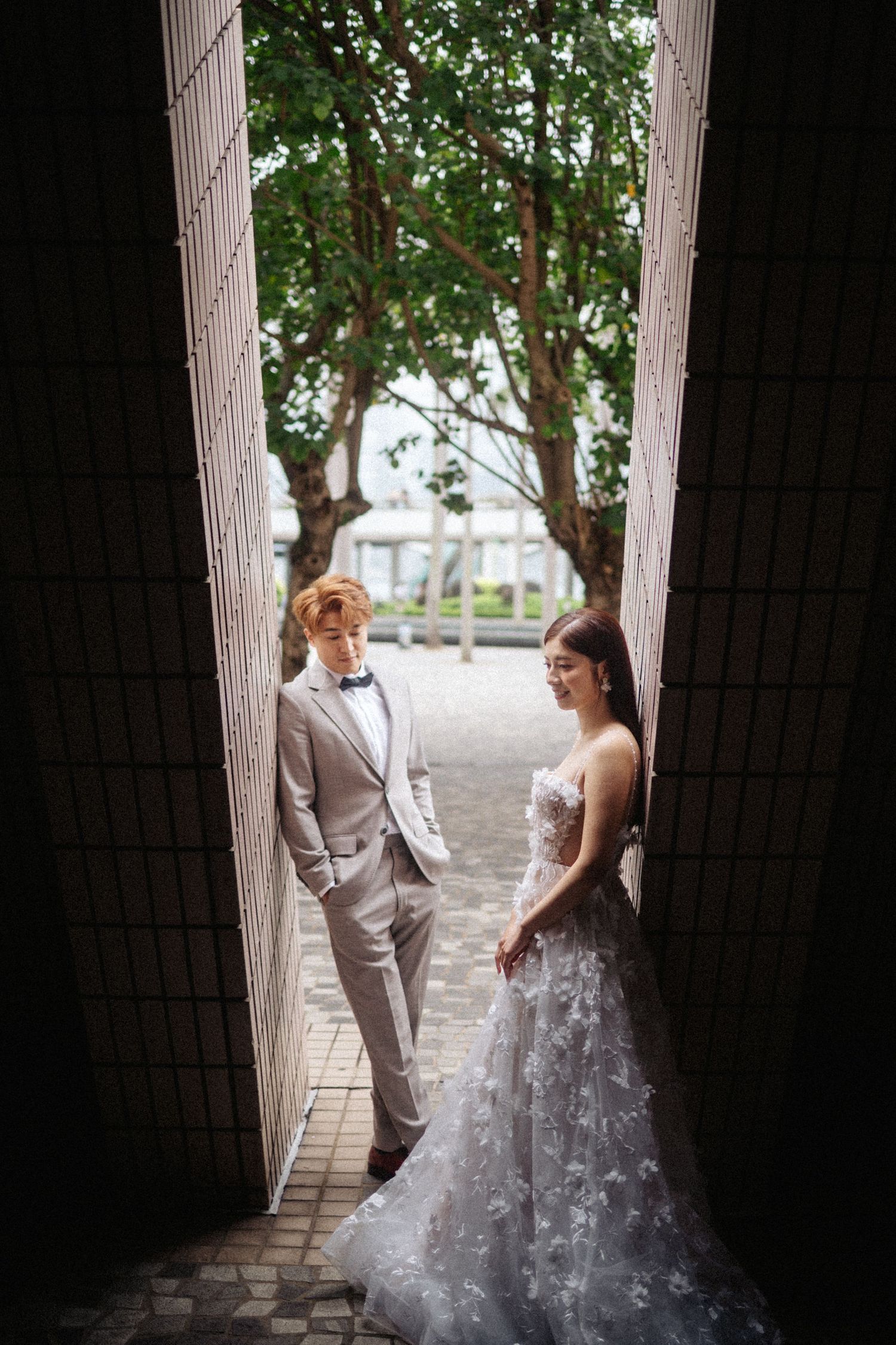 Bride and groom stand facing each other framed by a narrow tiled doorway with trees behind.