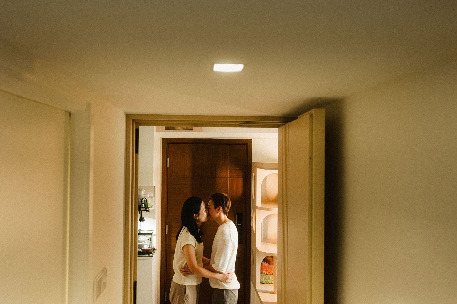 Couple standing close together in a doorway, framed by an open wooden door in warm light.