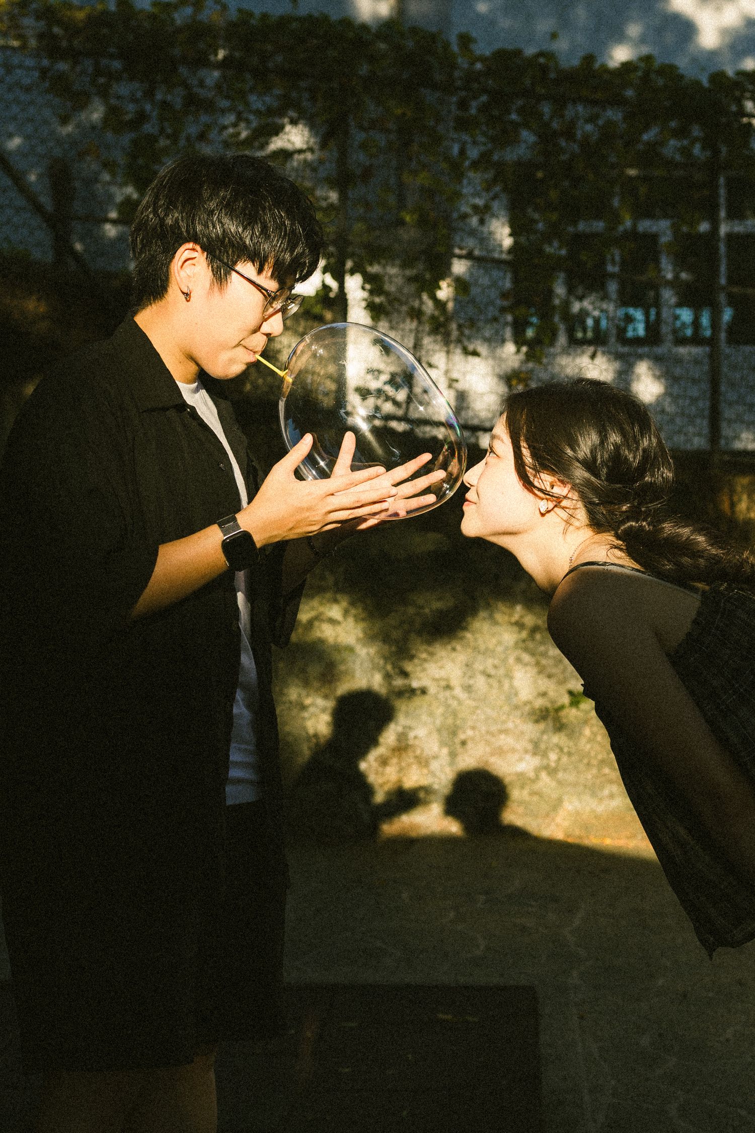 Young couple sharing a large soap bubble in warm golden sunlight with shadow on wall.
