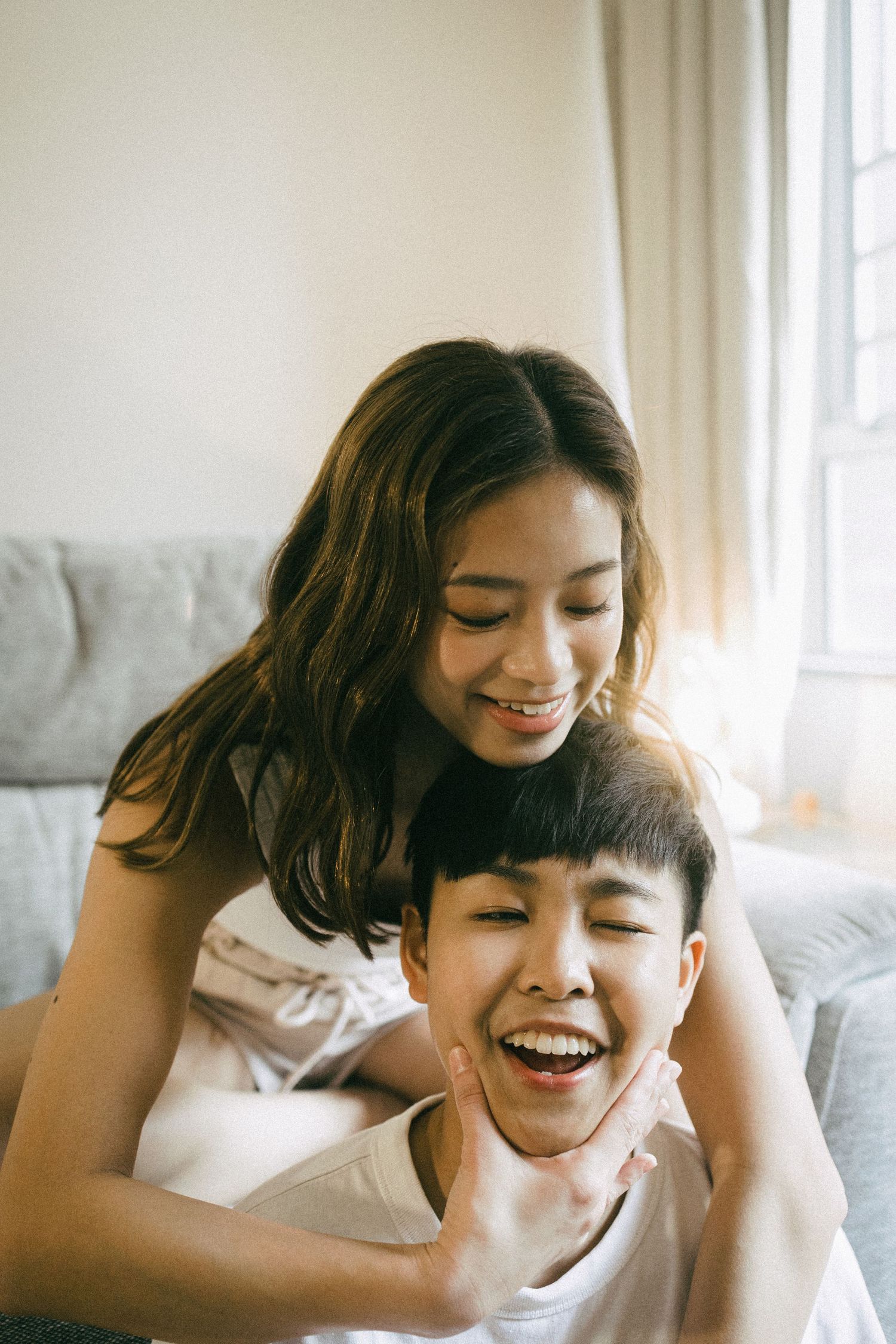 A happy Asian couple laughing and cuddling together on a couch in a bright living room.