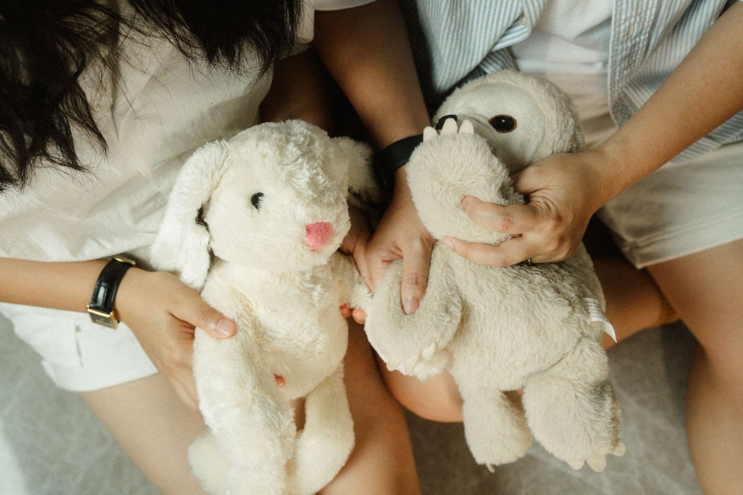 Two people sit together holding matching white stuffed bunny plush toys on their laps.