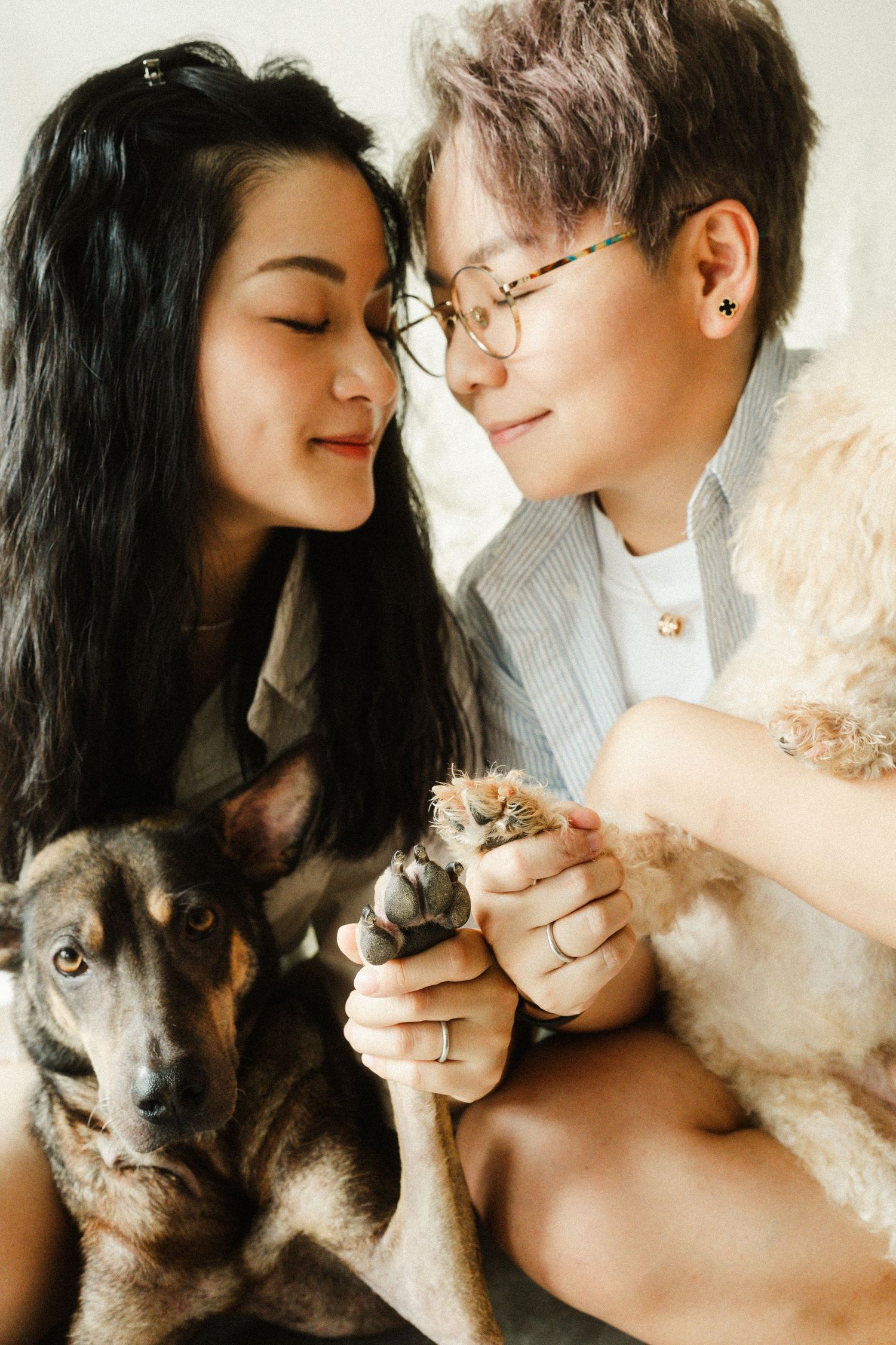 Two women share a tender moment with their dogs, holding a succulent plant together indoors.