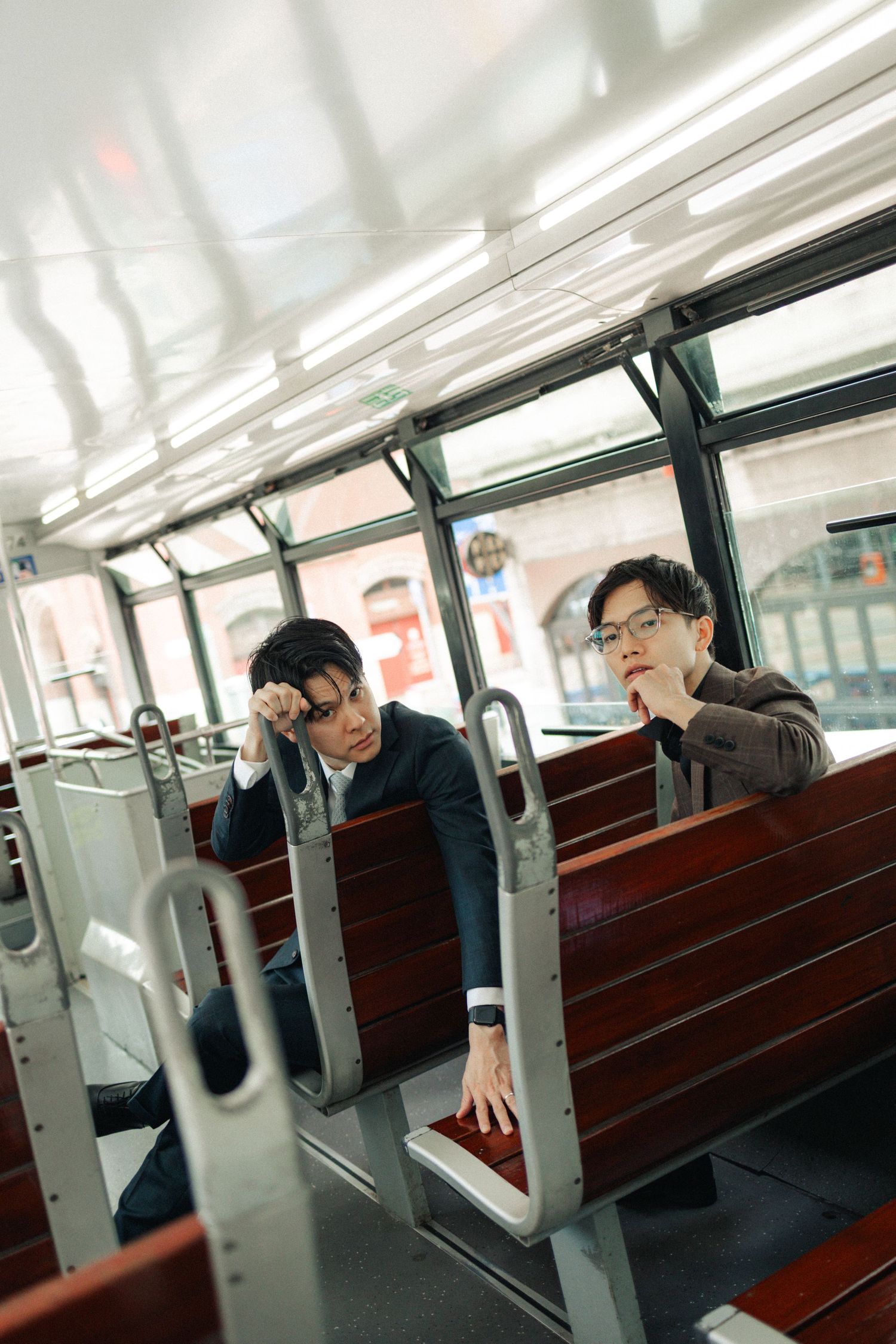 Two young Asian men sitting on vintage wooden tram seats looking thoughtfully out the window.