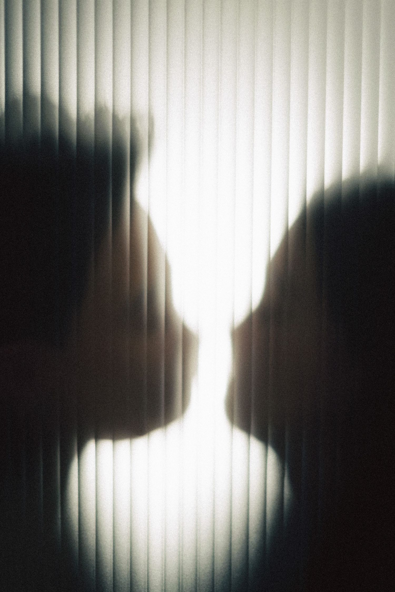 Silhouettes of two people facing each other through frosted glass panel, creating dramatic backlit shadow effect.