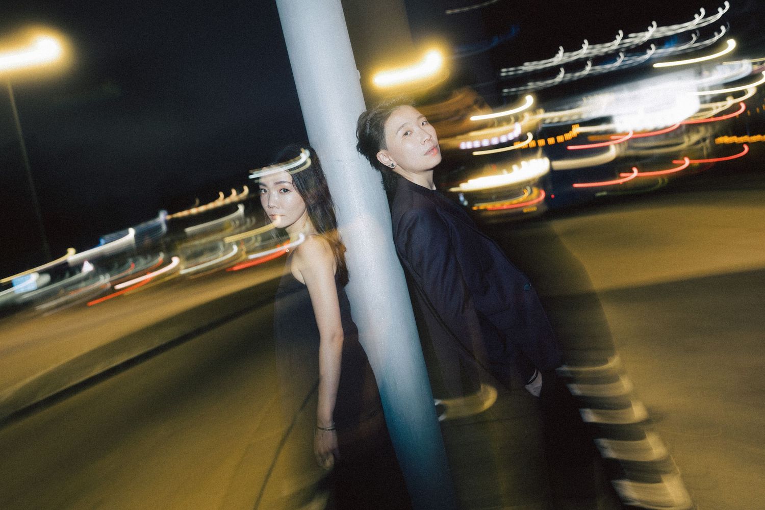 Couple playfully poses around a street pole at night with colorful bokeh city lights in the background.
