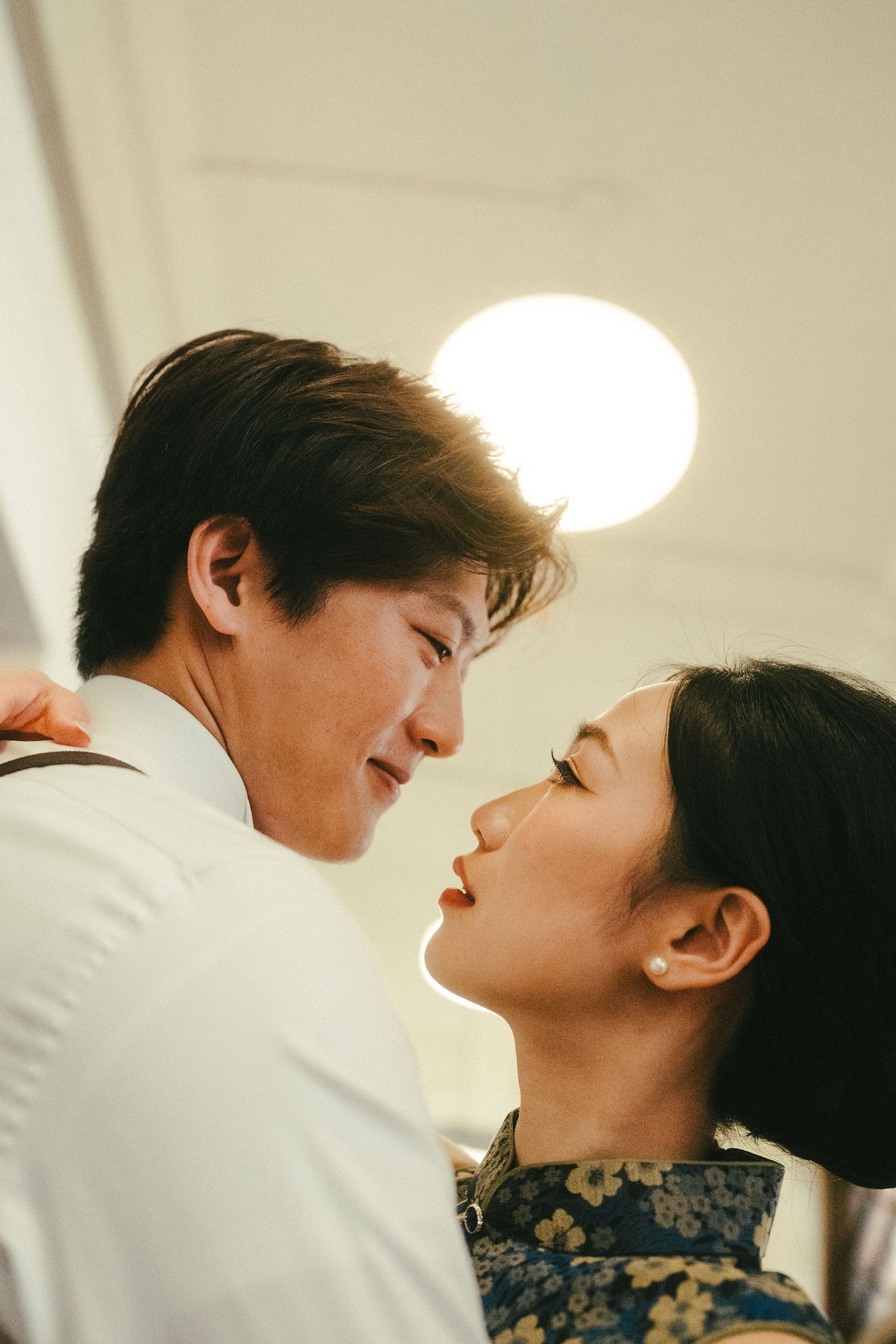 Romantic Asian couple sharing an intimate moment, faces close together under warm light.