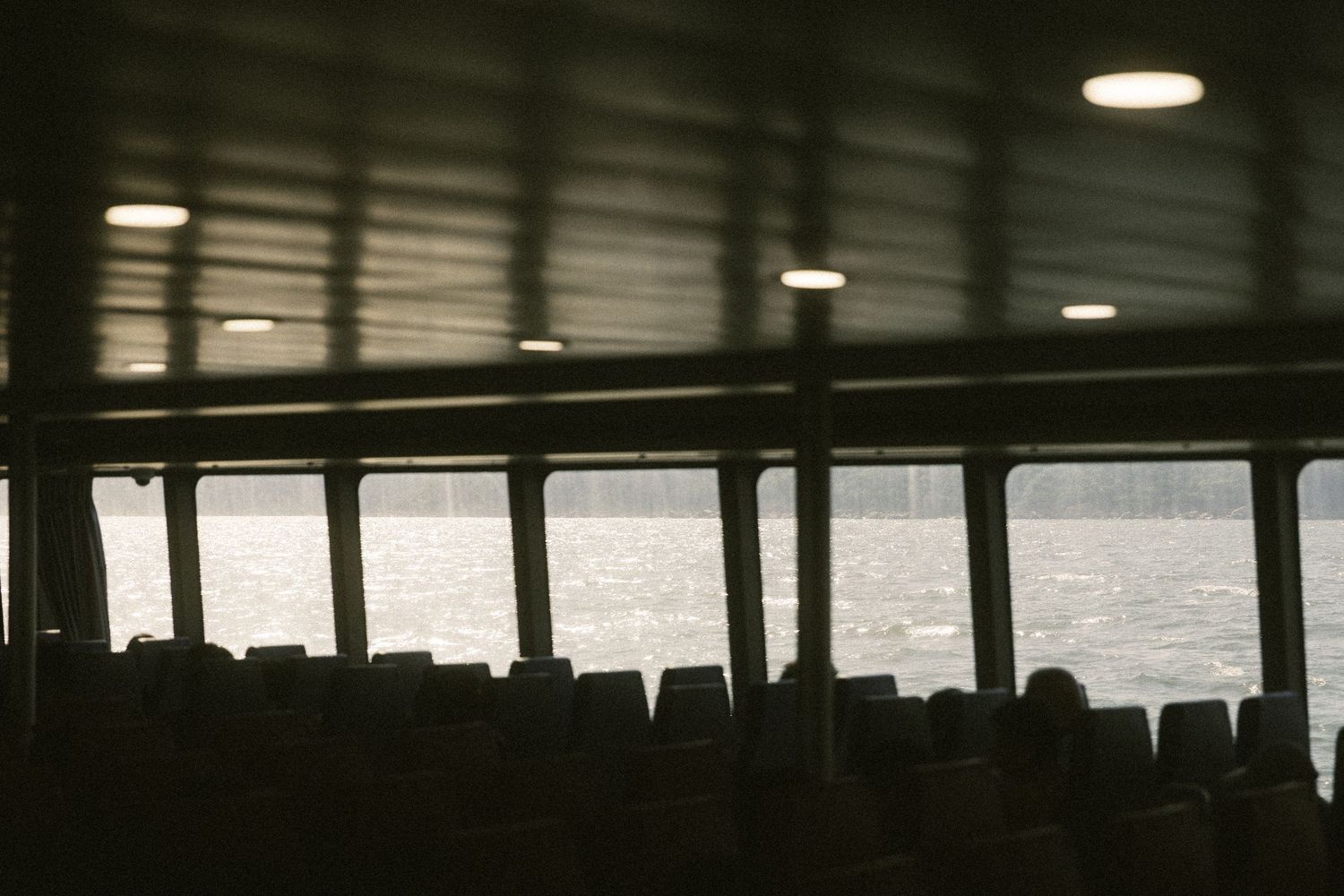 Silhouette of empty seats inside a dimly lit ferry cabin with ocean views through windows.