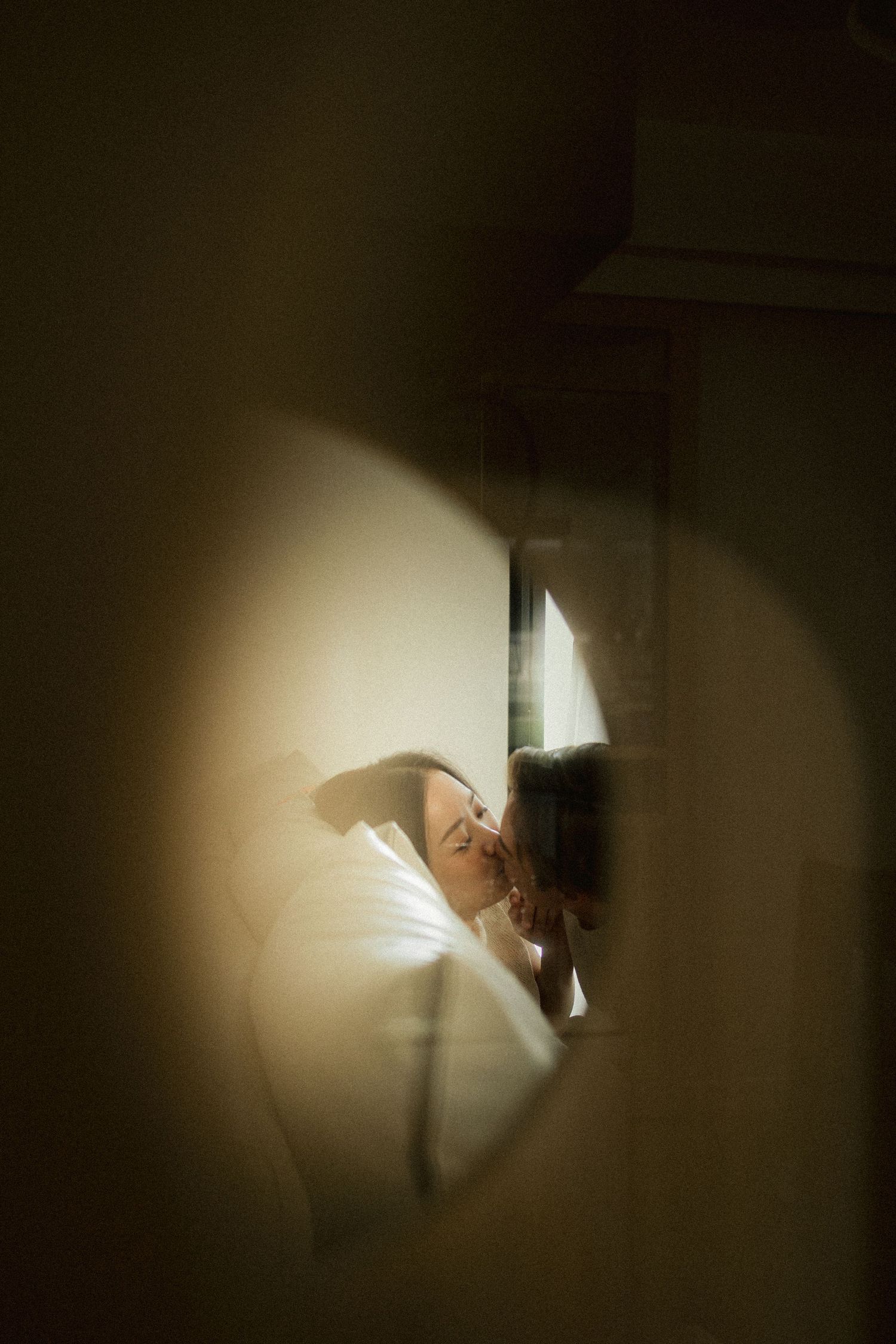 Couple sharing a tender kiss seen through a heart-shaped mirror reflection in soft warm light.