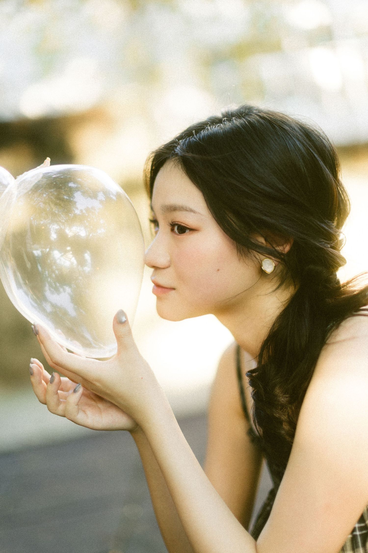 Young Asian woman gently kissing a large transparent soap bubble in soft bokeh light.