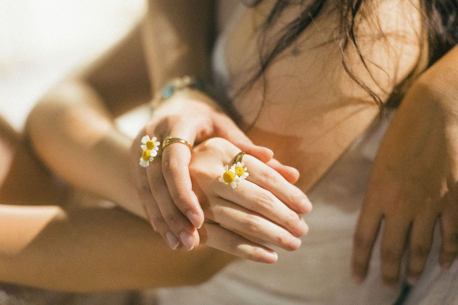 Close-up of two people holding hands adorned with delicate daisy flower rings.
