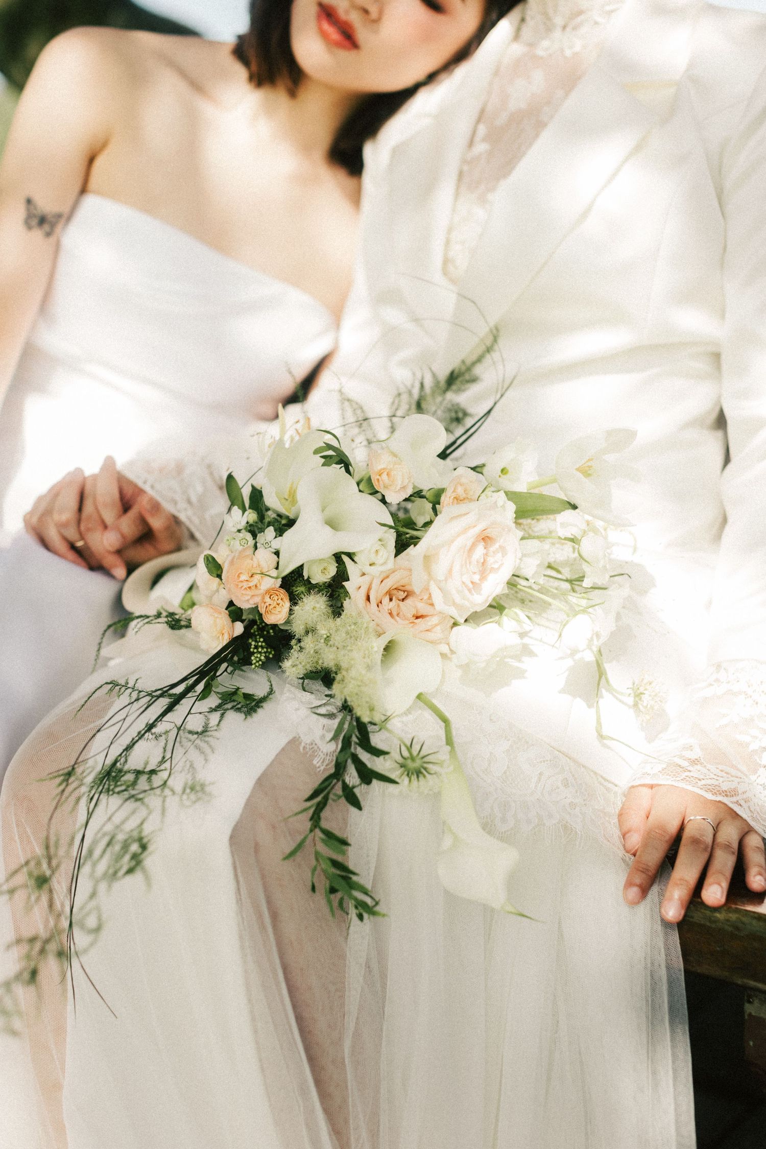 Close-up of two brides holding a cascading bridal bouquet of white and blush roses with greenery accents.