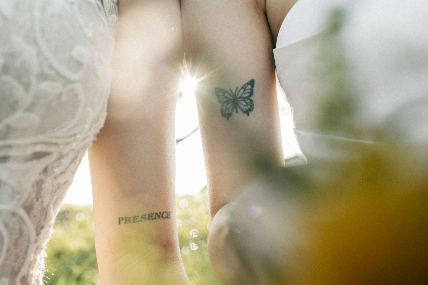 Close-up of a bride's leg showing a butterfly tattoo and word tattoo in sunlight.