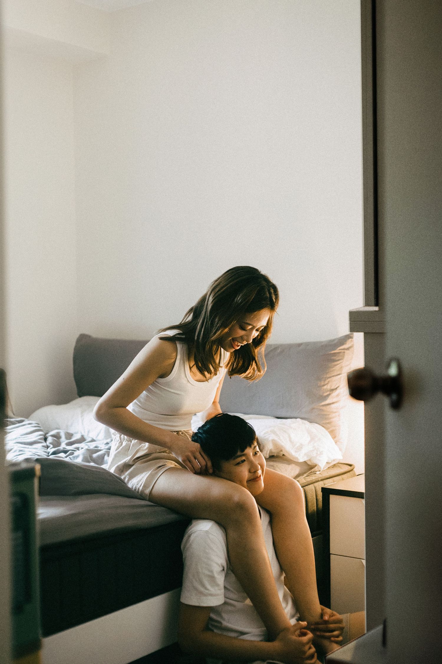 A woman sitting on a bed smiling down at a man resting his head on her lap in a cozy bedroom.