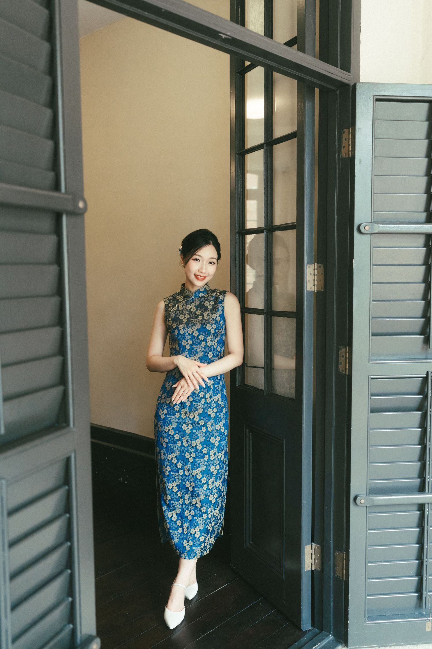 Beautiful Asian woman in traditional blue floral cheongsam qipao dress standing in doorway.