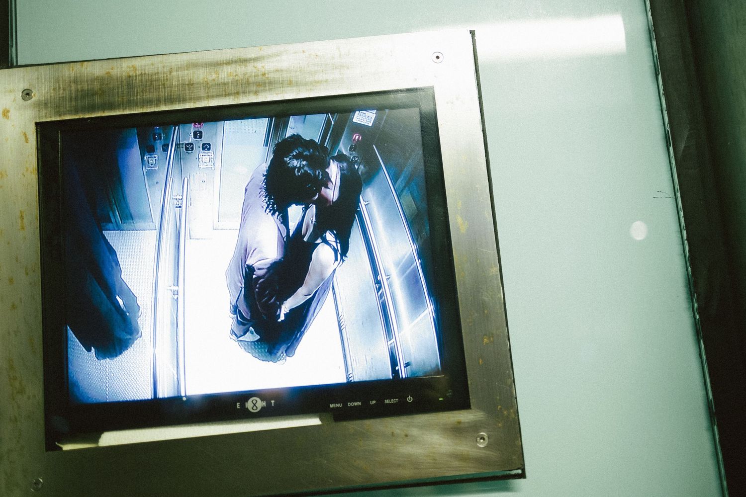 Security monitor displaying a person inside an elevator in a building lobby.
