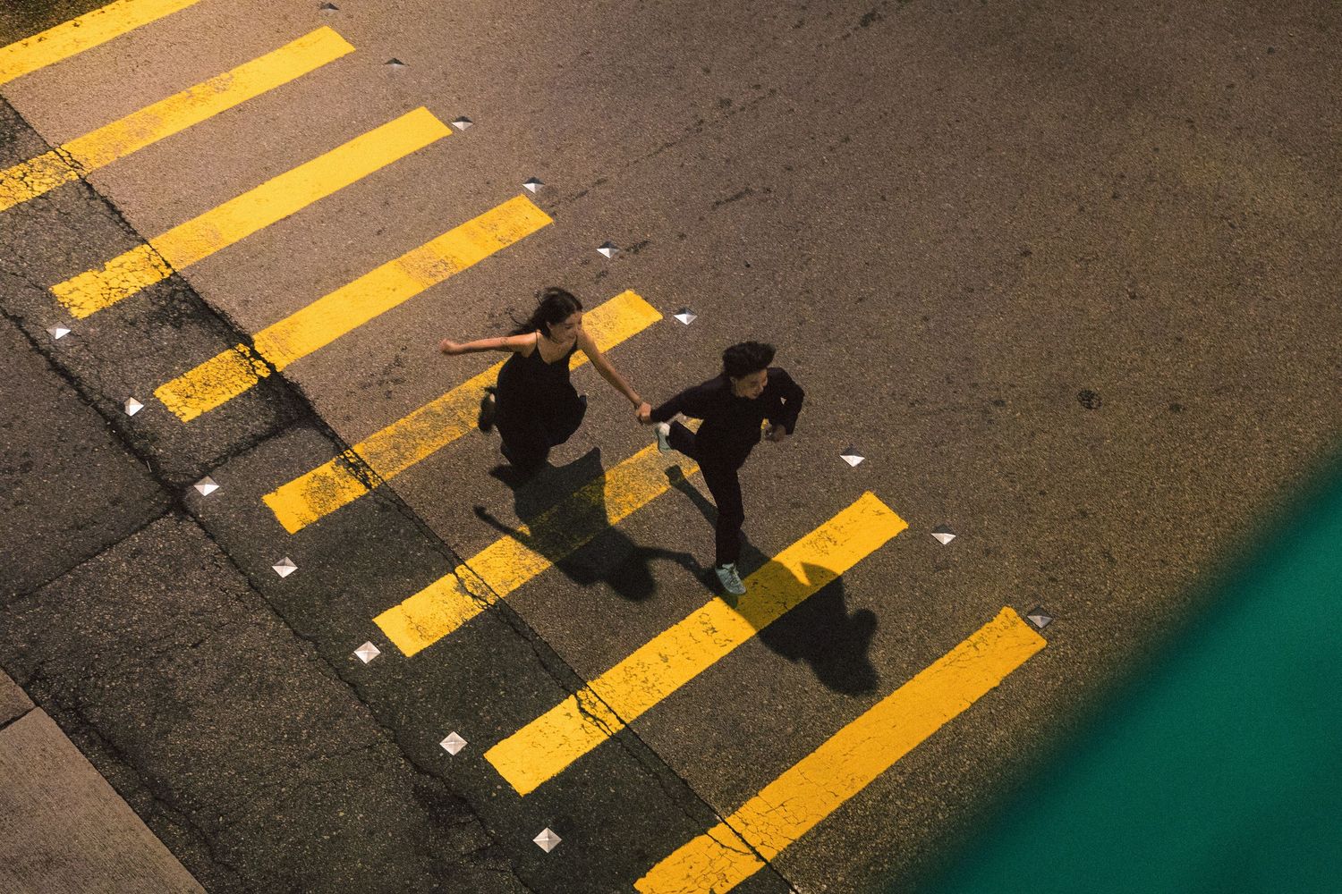 Aerial view of two people crossing a bright yellow zebra crossing at night.